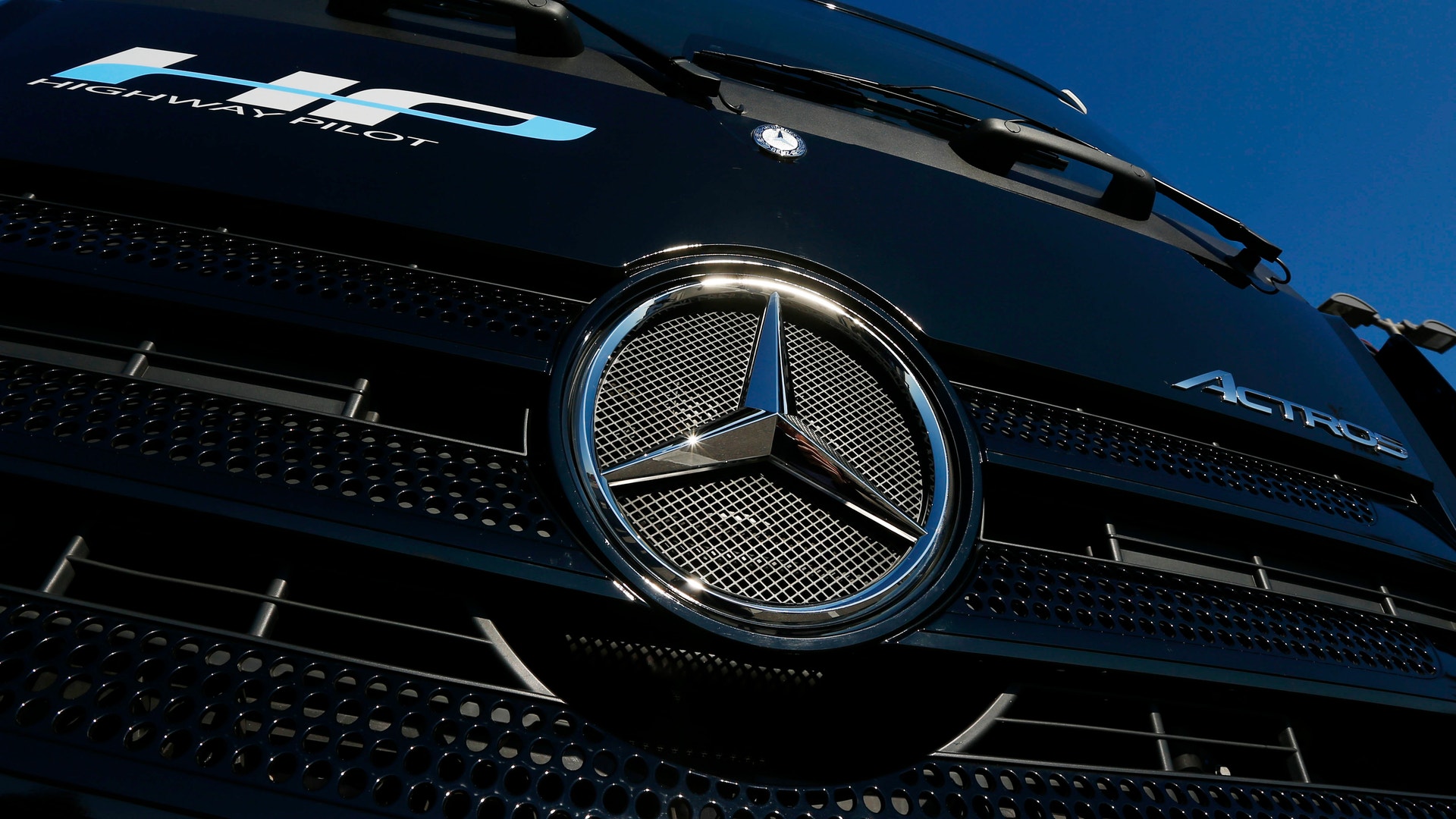 Närbild på Mercedes-Benz lastbils grille med den karakteristiska trestjärniga logotypen mot blå himmel.