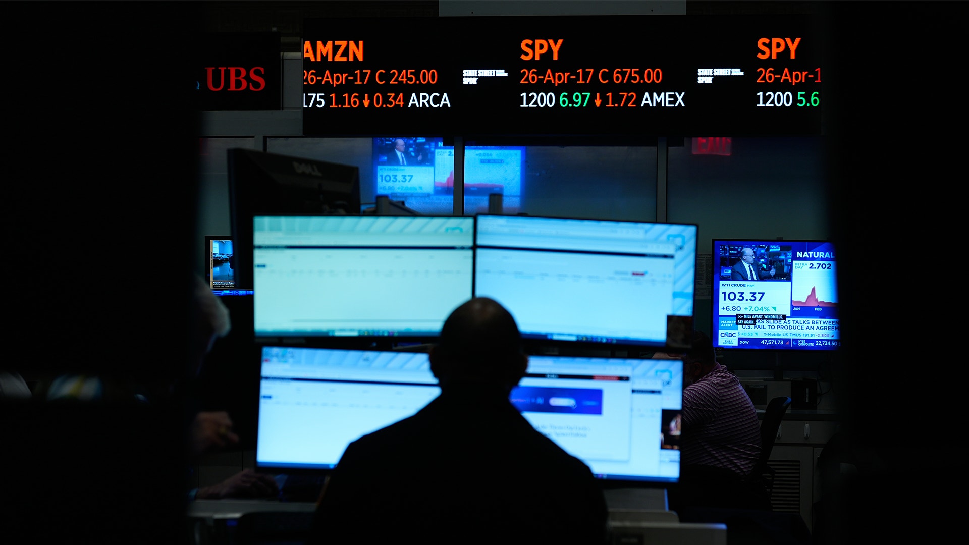 En trader sitter framför flera datorskärmar med aktiekurser och marknadsdata på Wall Street.