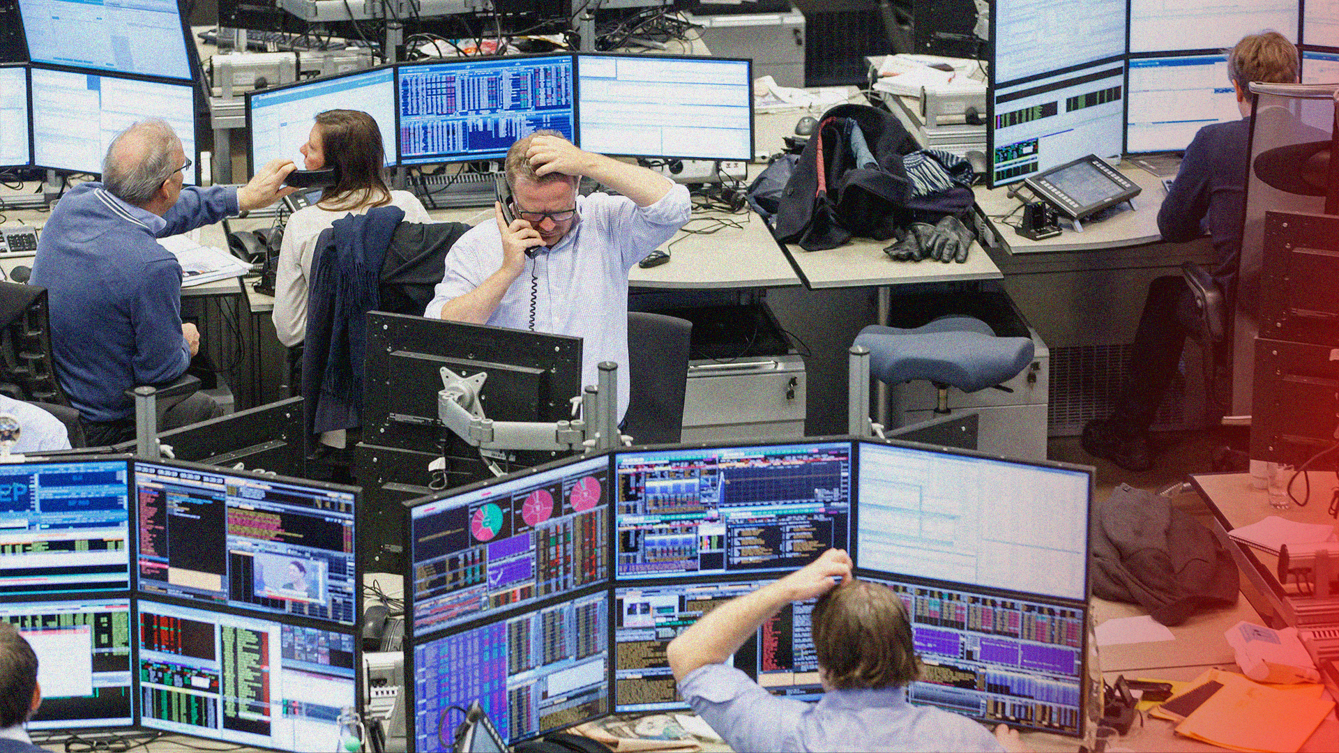 Handelsplats med flera personer som arbetar vid skrivbord med flera datorskärmar som visar finansiell data och diagram.