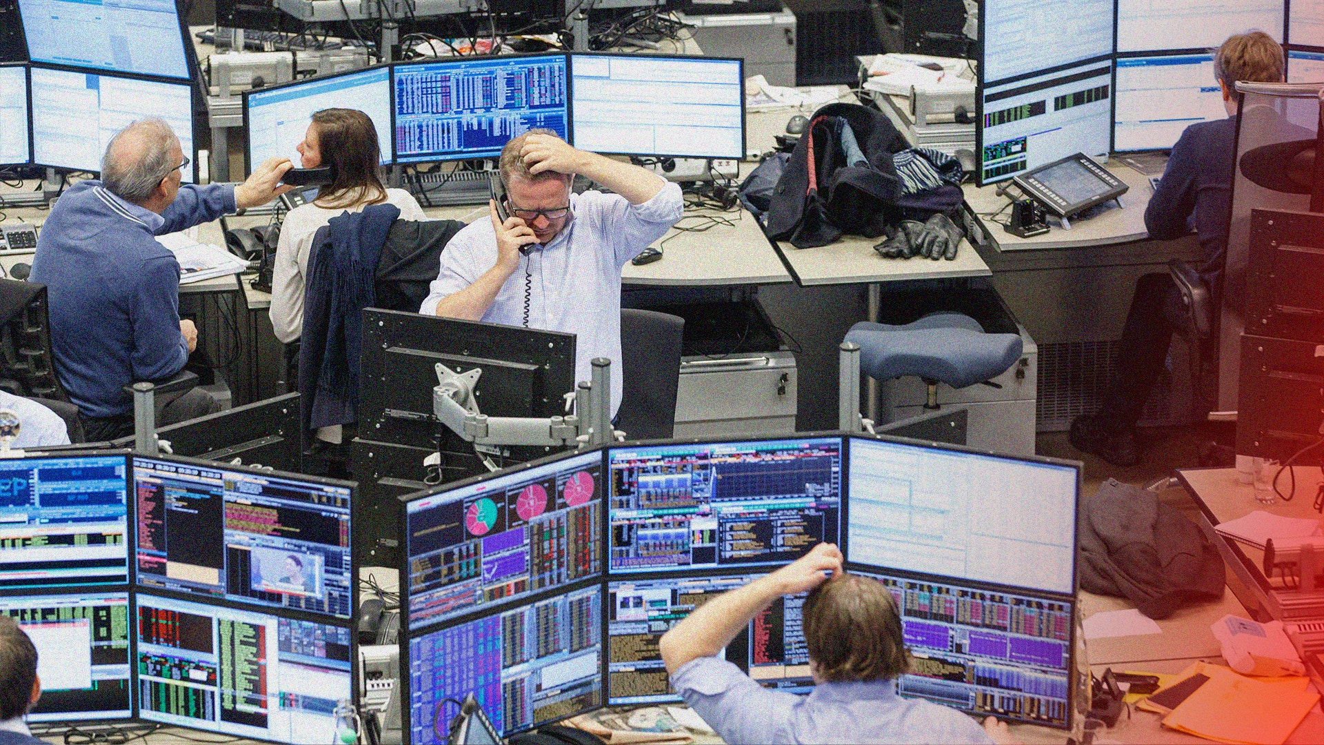 Handelsplats med flera personer som arbetar vid skrivbord med flera datorskärmar som visar finansiell data och diagram.