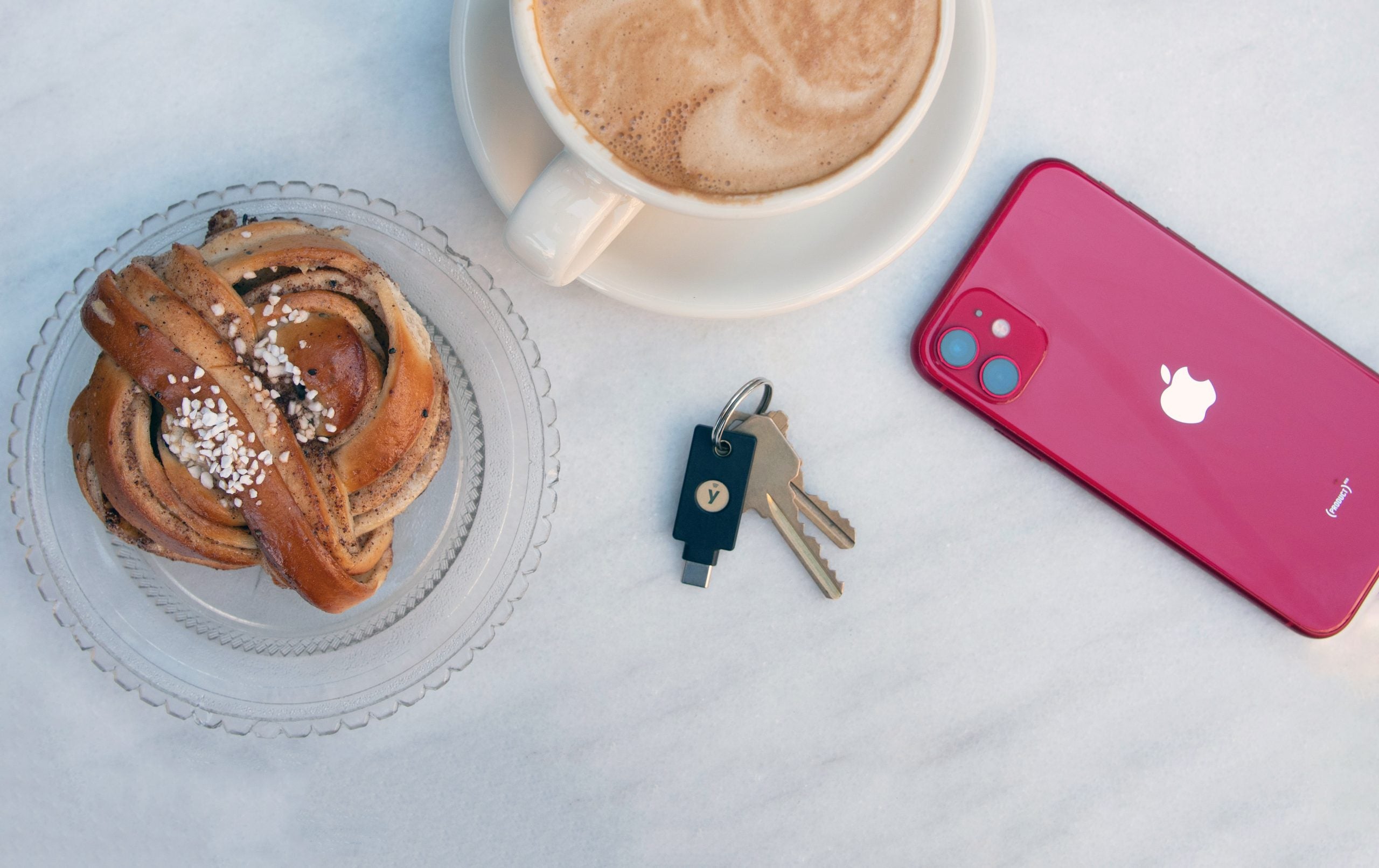 Kanelbulle, en kopp kaffe, nycklar och en mobiltelefon på ett bord.