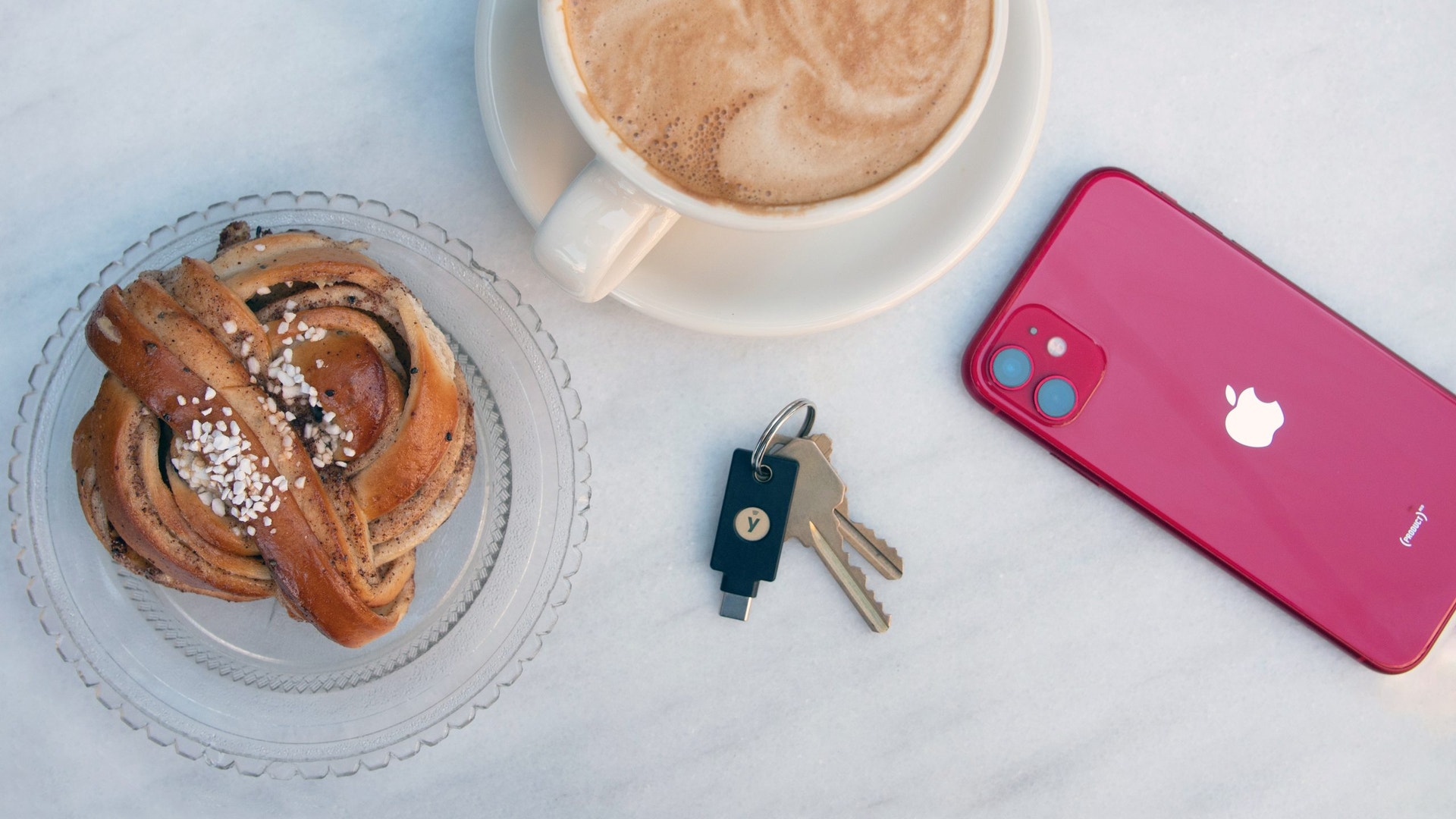 Kanelbulle, en kopp kaffe, nycklar och en mobiltelefon på ett bord.