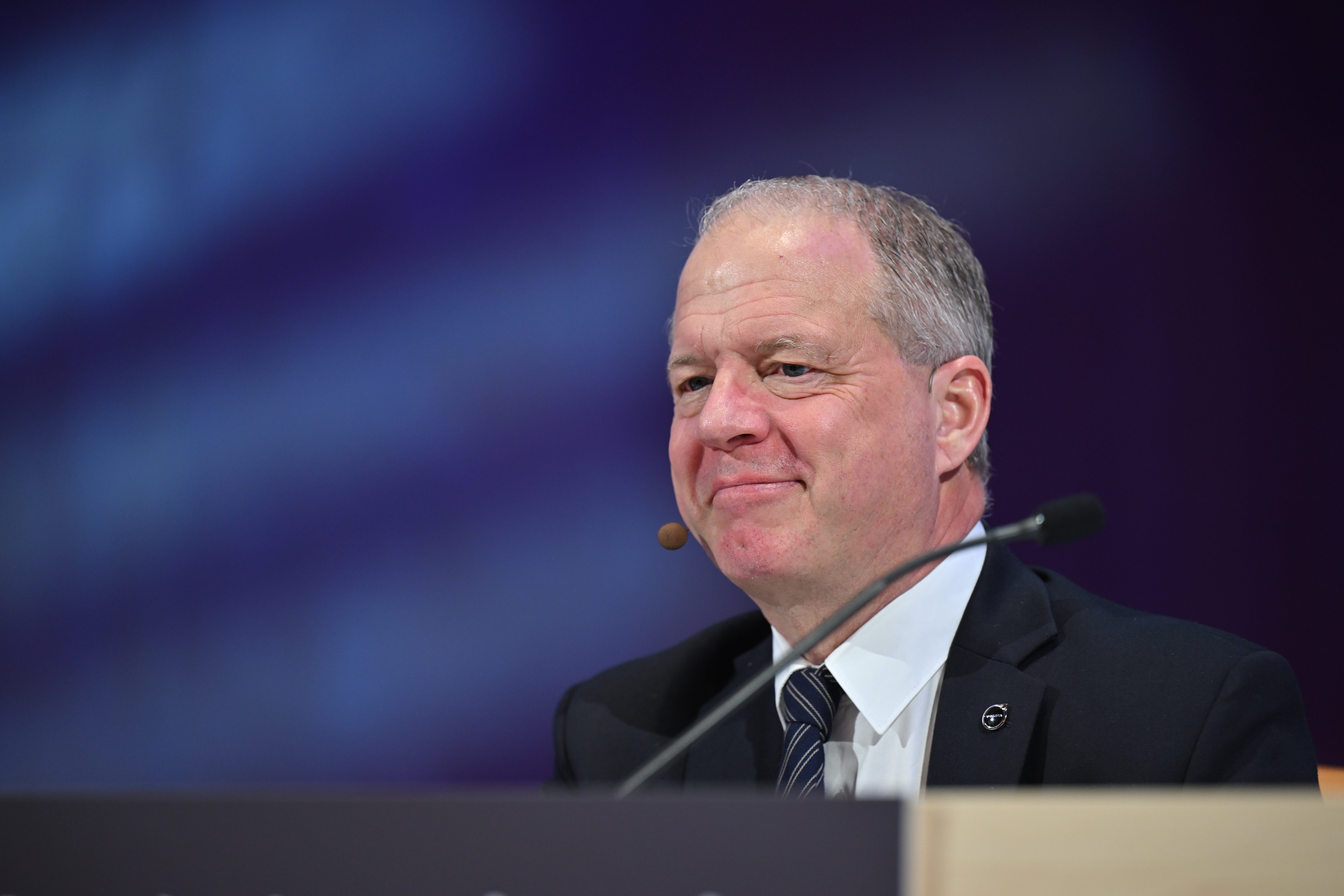 En man i kostym talar vid en mikrofon under en konferens eller offentlig event.