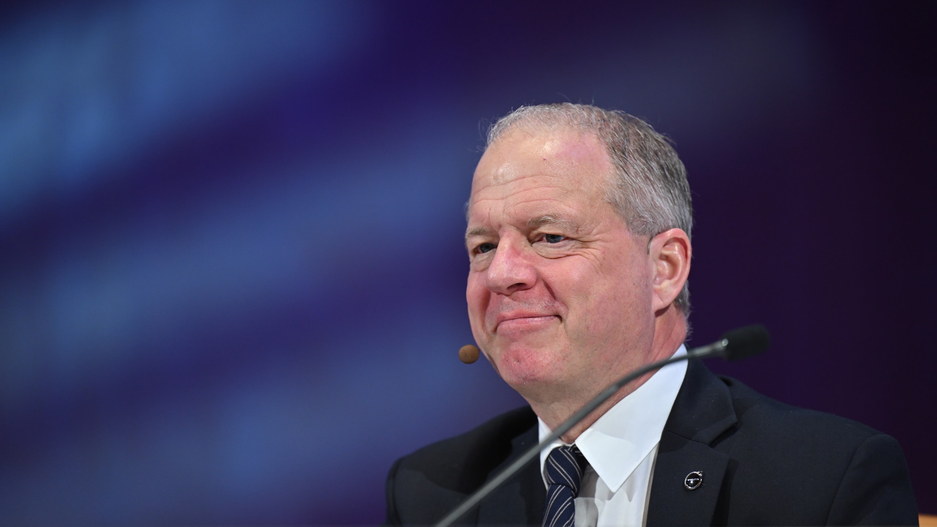 En man i kostym talar vid en mikrofon under en konferens eller offentlig event.