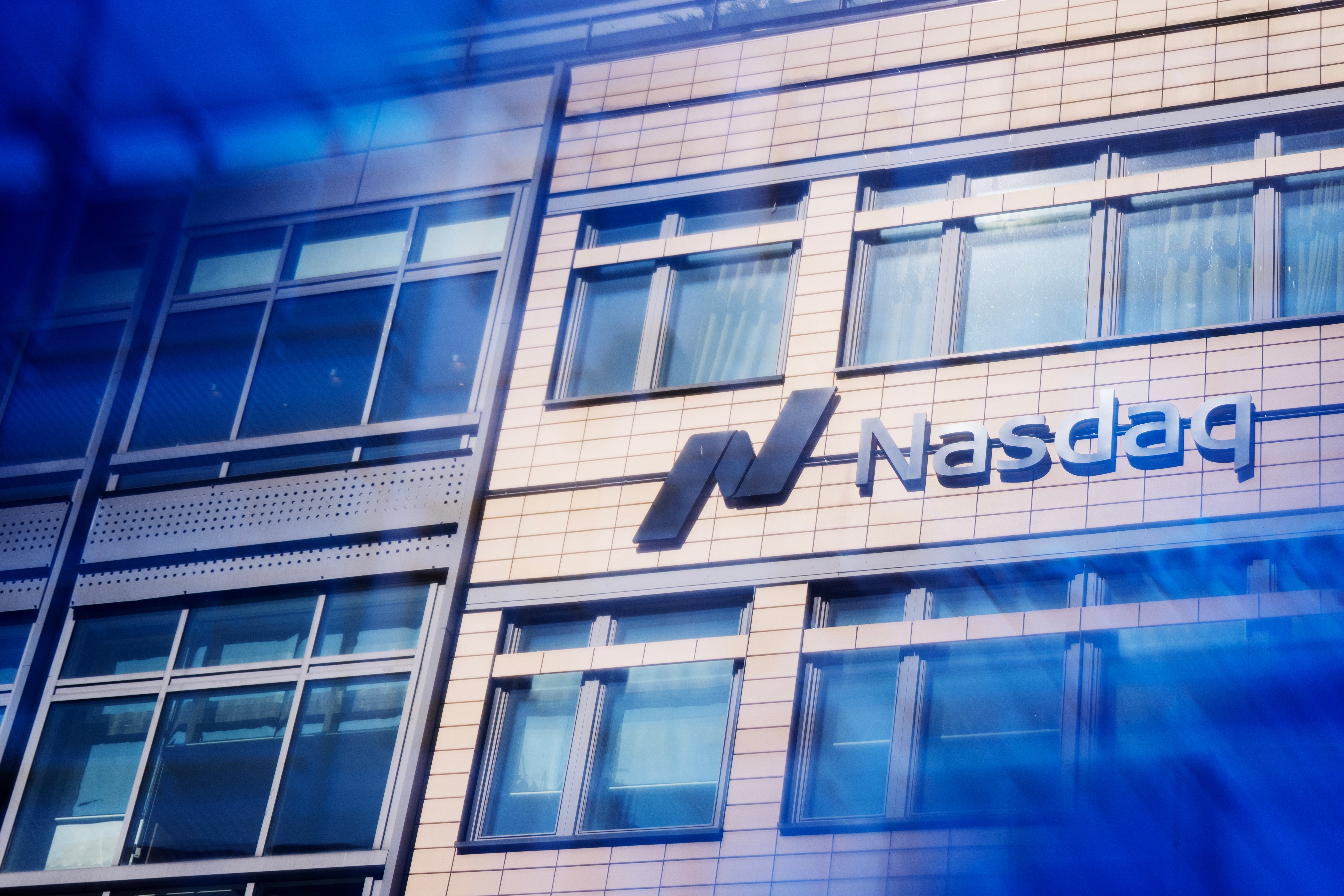 Nasdaq-logon på en modern byggnads fasad med stora fönster och blå belysning.