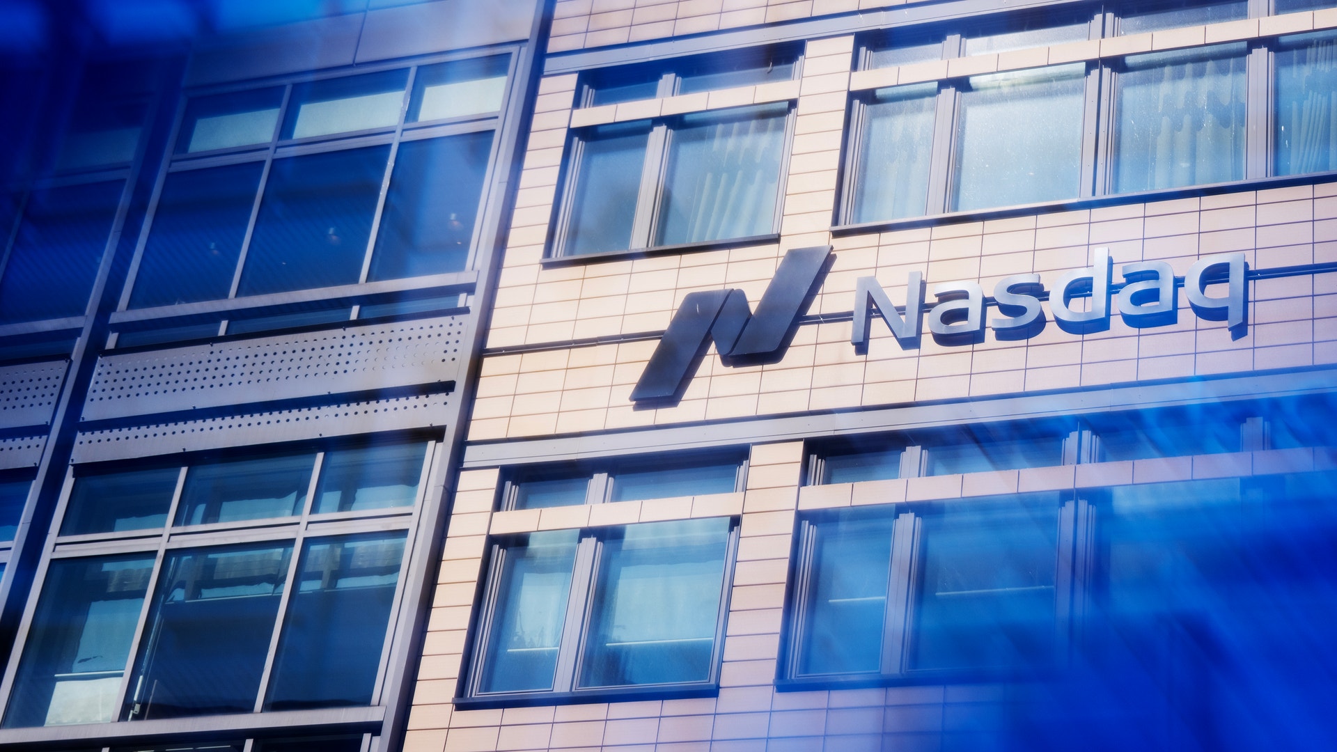 Nasdaq-logon på en modern byggnads fasad med stora fönster och blå belysning.