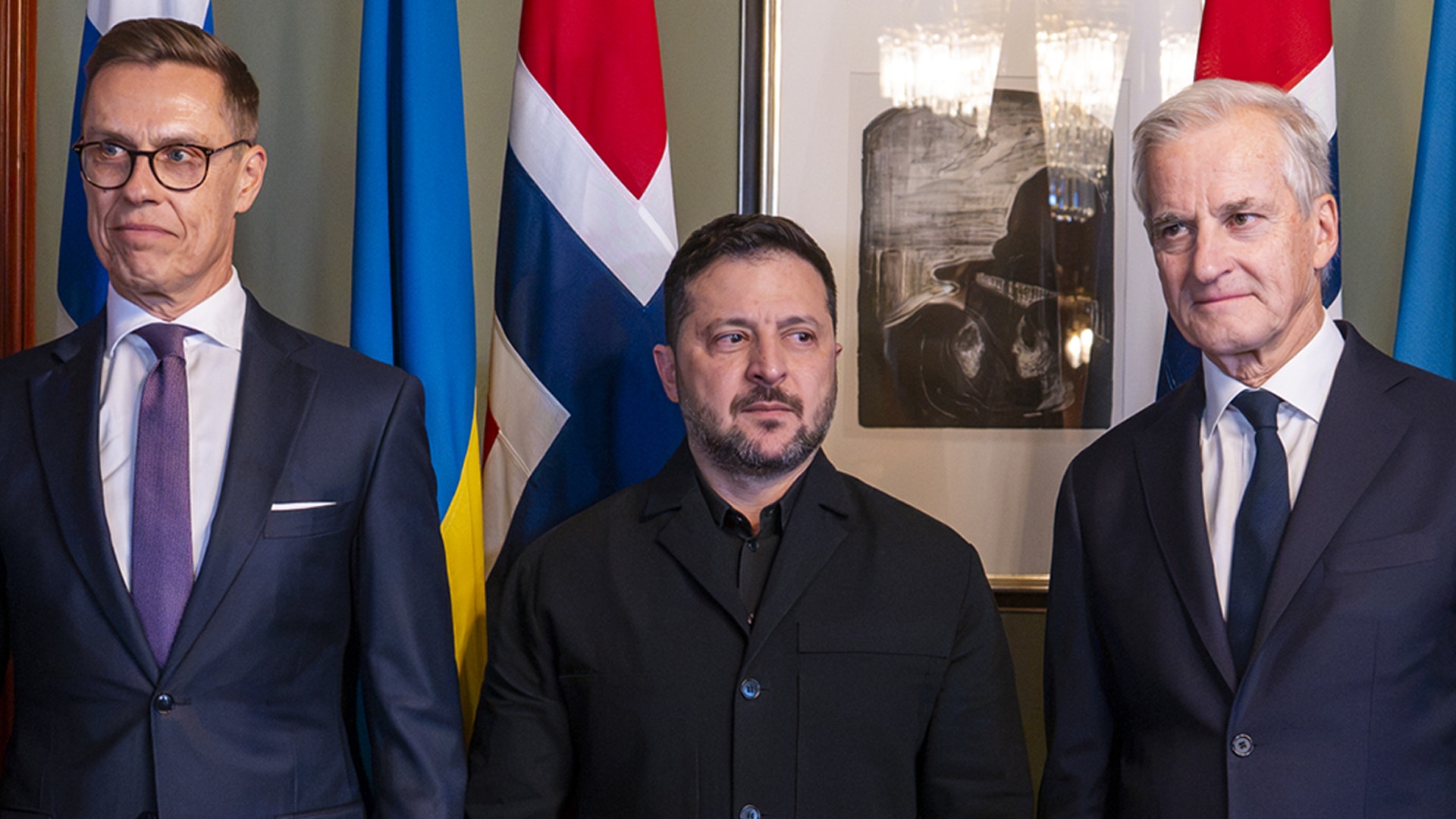 Tre män i mörka kläder står bredvid varandra framför flera flaggor, bland annat Sveriges och Norges.