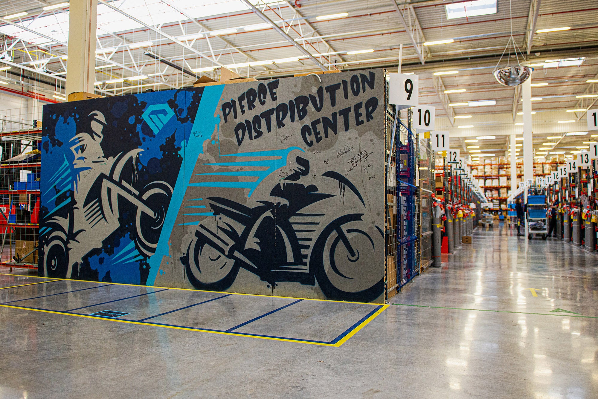 Väggmålning i ett distributionscenter med blå och svart konst som visar cykelåkare och cyklar, med texten Pipoe Distribution Center.