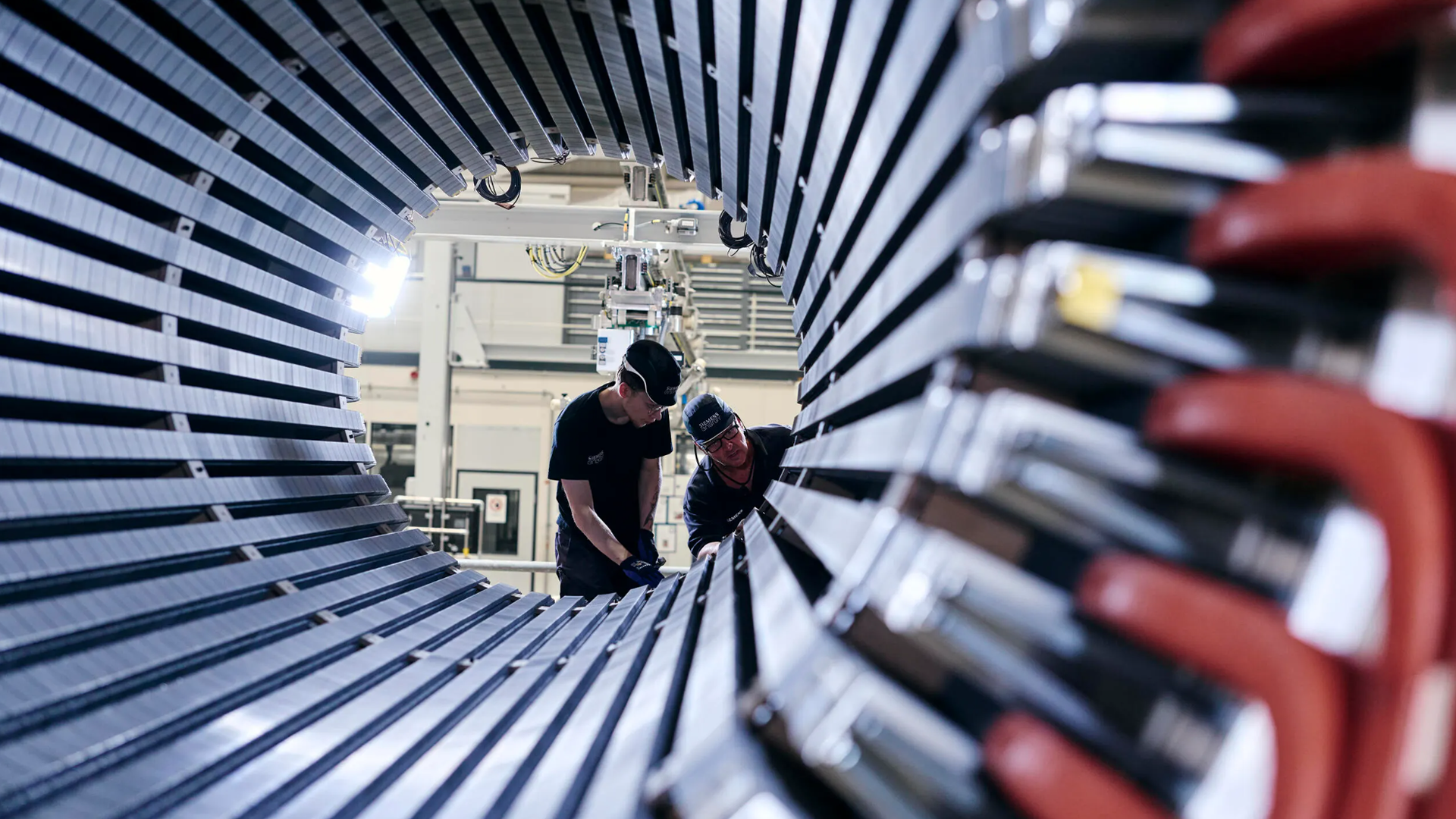 Två arbetare inspekterar en stor cylindrisk industriell komponent från insidan, fotograferad genom metalliska radiella linjer.