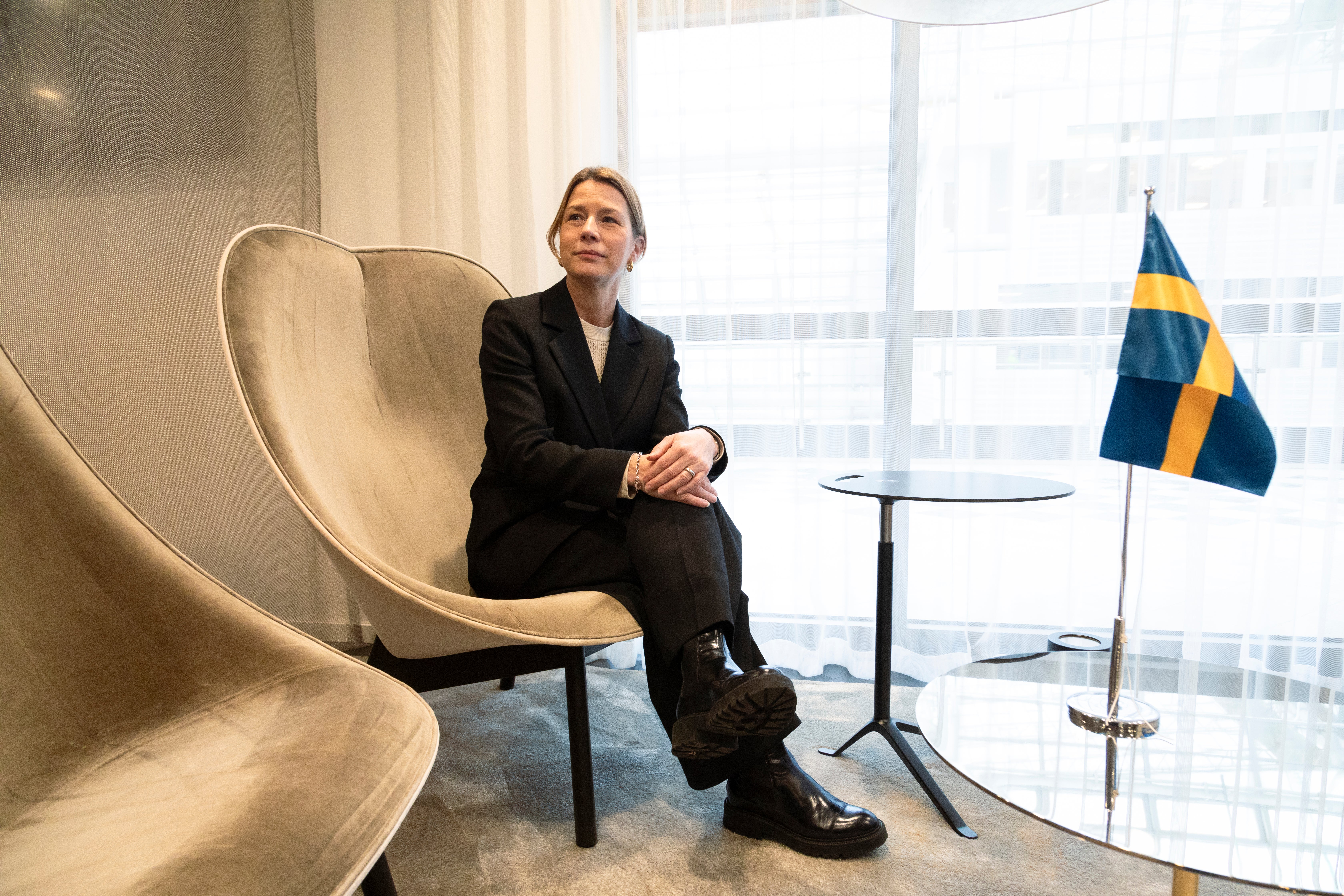 Business Swedens chefsekonom Lena Sellgren bredvid en svensk flagga som står på ett glasbord.
