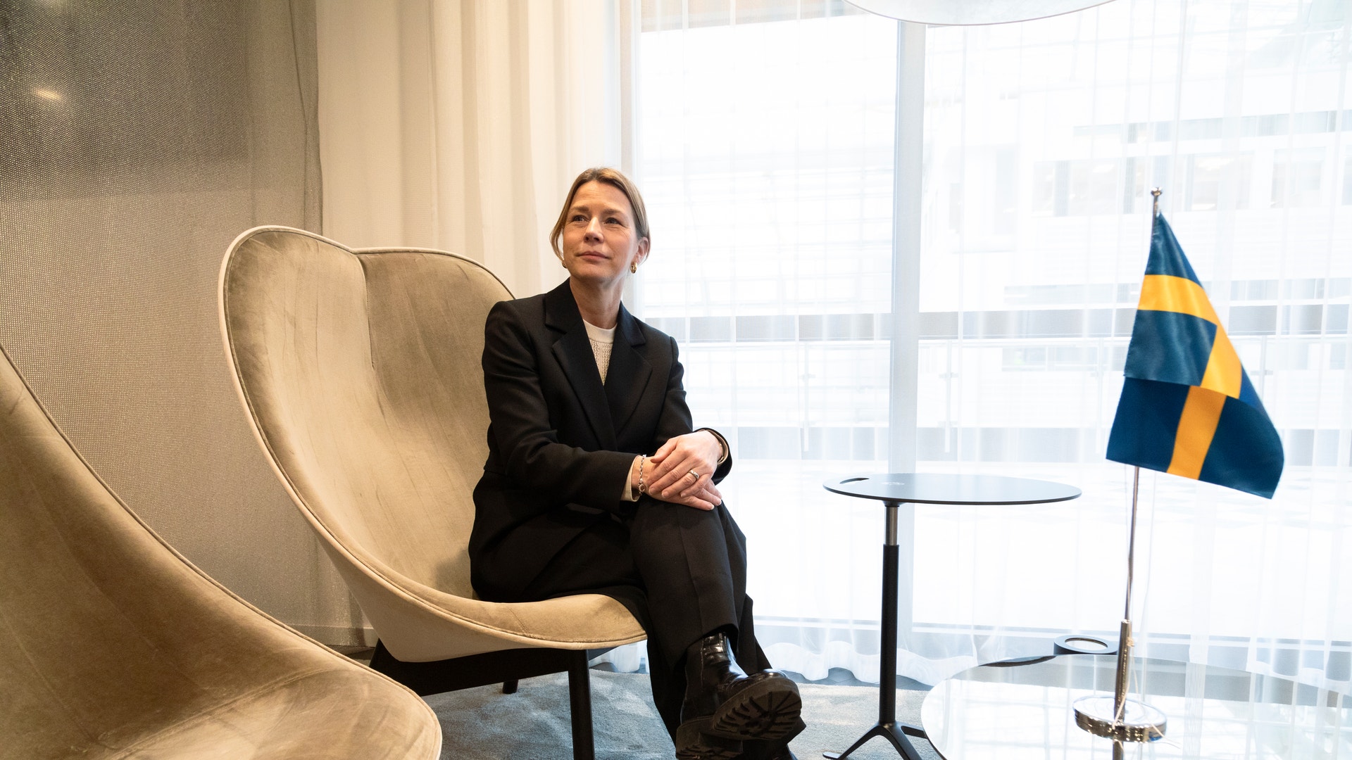 Business Swedens chefsekonom Lena Sellgren bredvid en svensk flagga som står på ett glasbord.