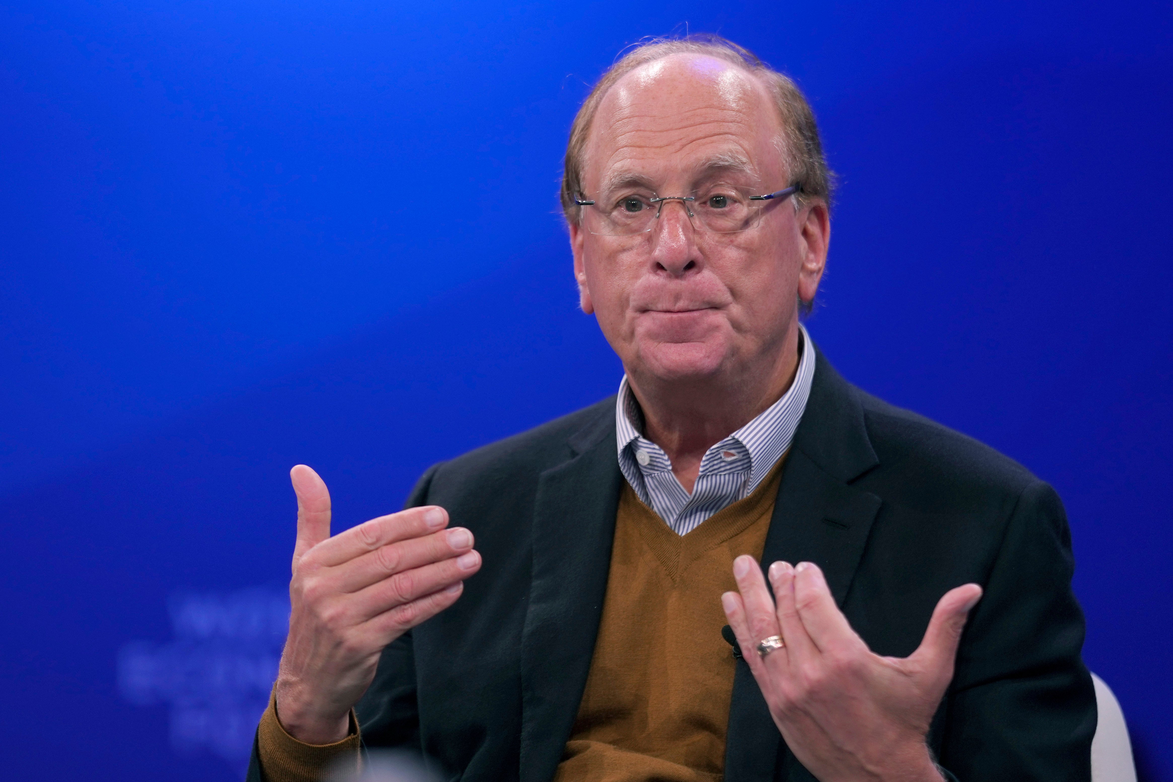 Larry Fink, en äldre man med glasögon och mörk kavaj, gestikulerar med båda händerna medan han pratar framför en blå bakgrund.