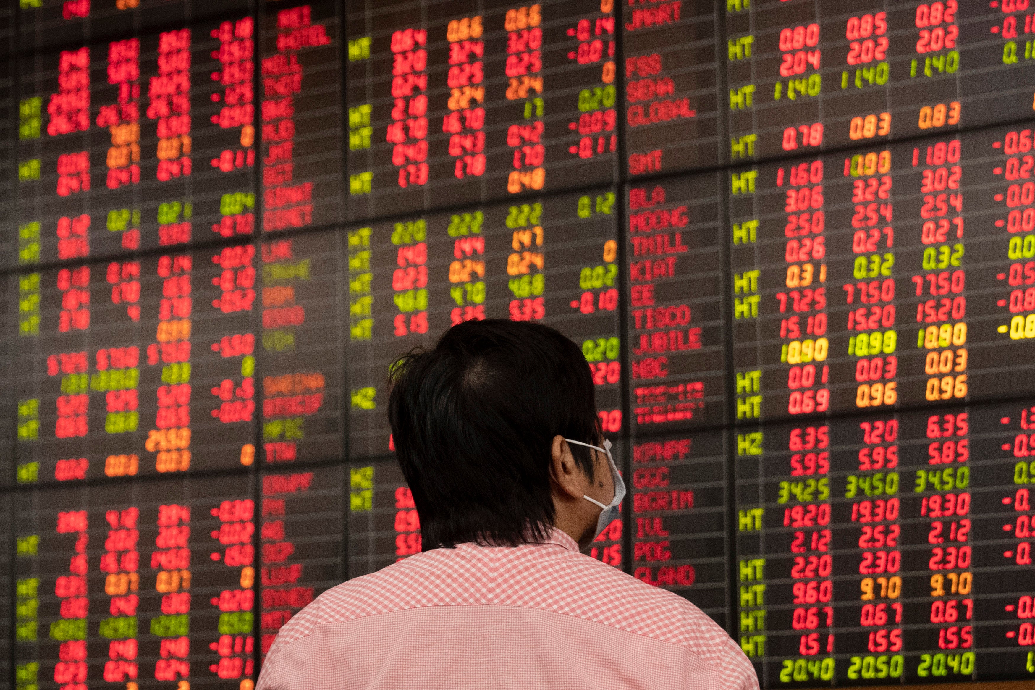 Person som tittar på en aktiemarknadstavla med röda och gula siffror som visar finansiell data.