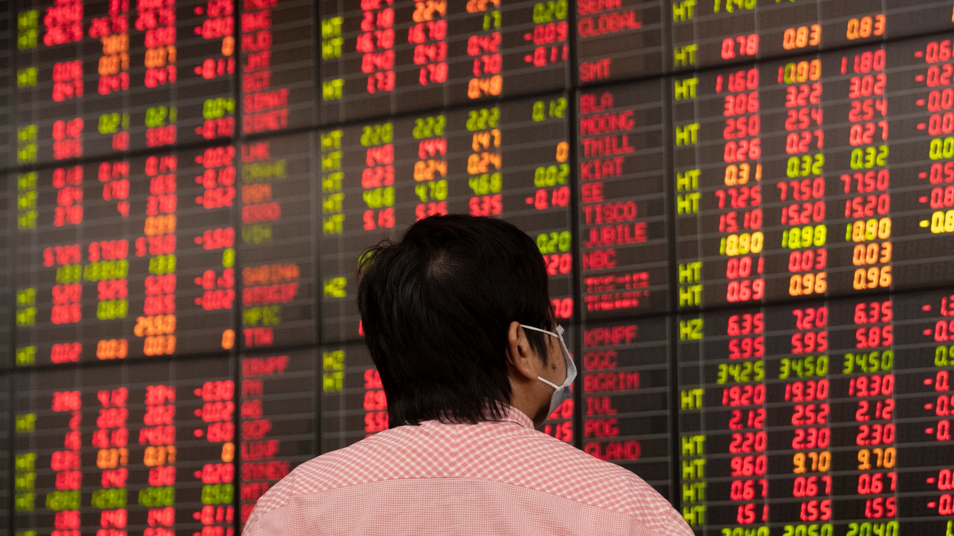 Person som tittar på en aktiemarknadstavla med röda och gula siffror som visar finansiell data.