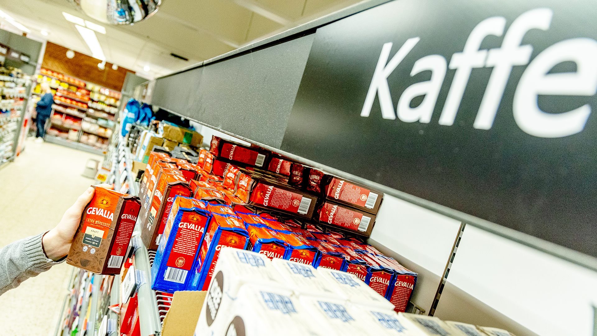 Kaffehylla i en matbutik med olika kaffepaketen på hyllorna och ett skyltat märkt 'Kaffe'.