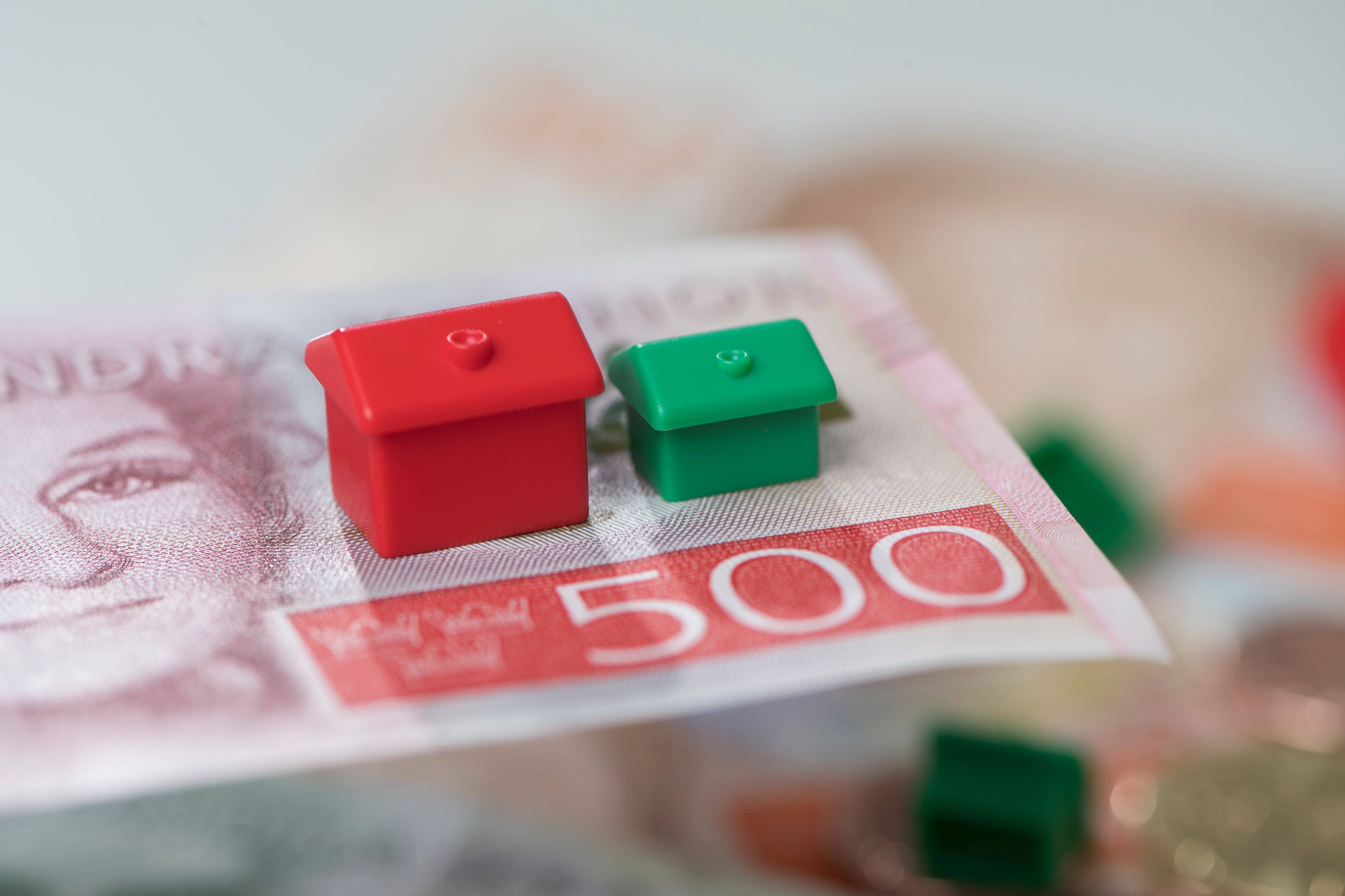 Två små husmodeller, en röd och en grön, placerade på ett eurosedel.