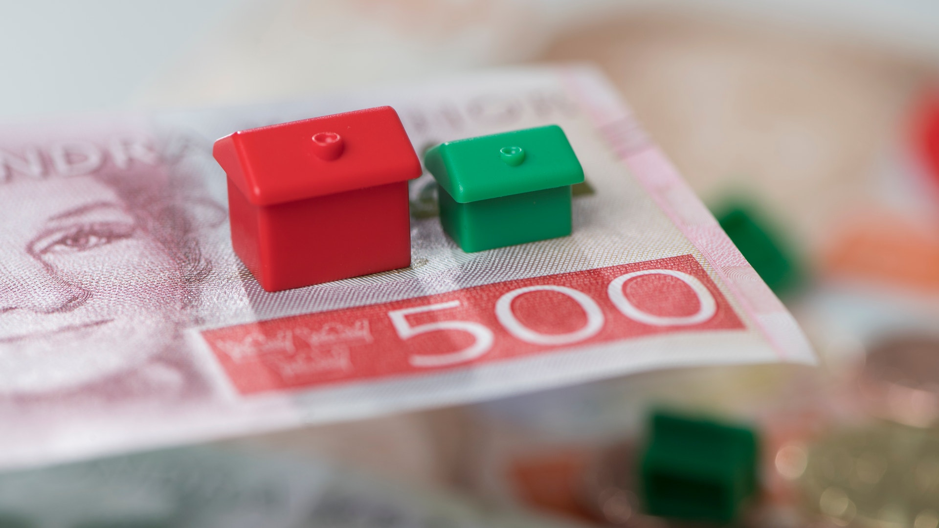 Två små husmodeller, en röd och en grön, placerade på ett eurosedel.
