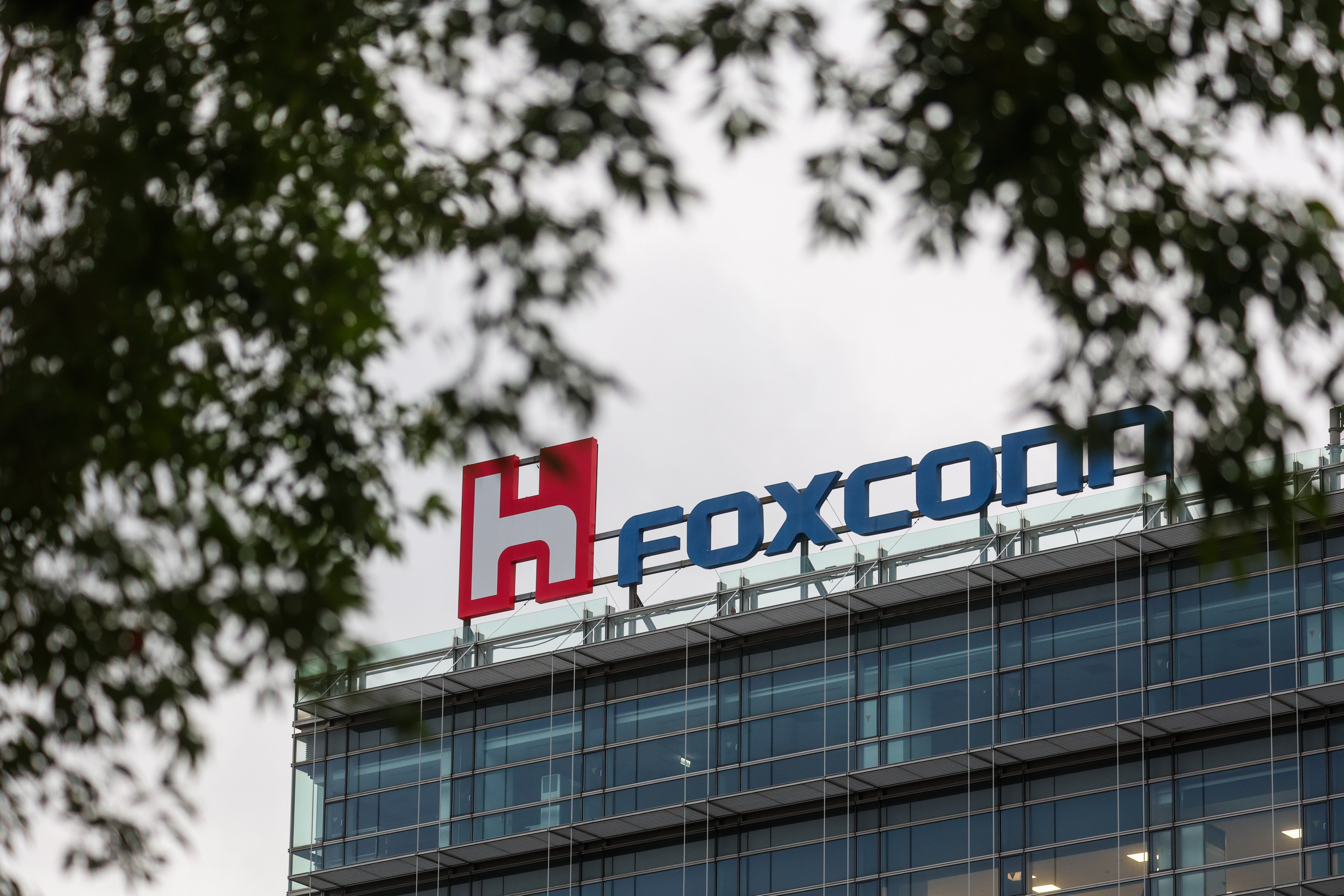 Kontorsbyggnad med Foxconn-logon på taket. Byggnaden har stora glasfönster och är omgiven av träd.
