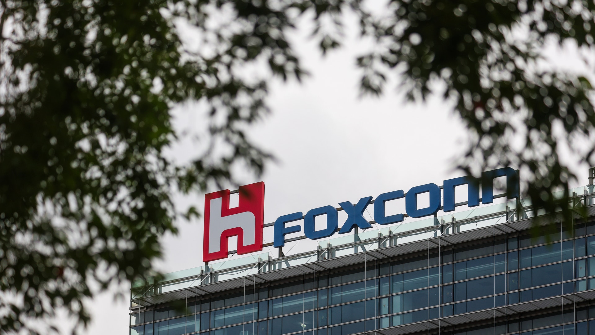 Kontorsbyggnad med Foxconn-logon på taket. Byggnaden har stora glasfönster och är omgiven av träd.