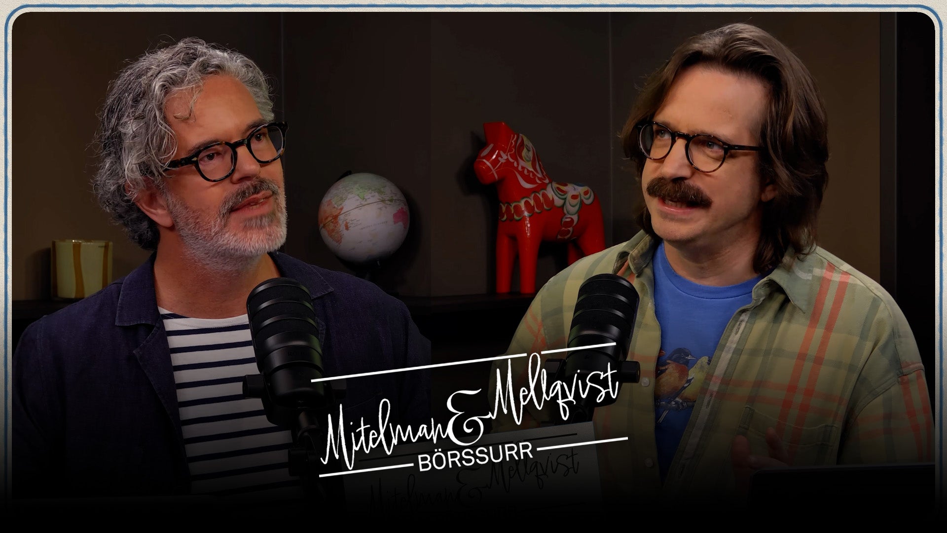 Två män sitter vid mikrofoner i en podcast- eller intervjustudio. De bär glasögon och ser mot sidan. I bakgrunden syns dekorativa föremål.