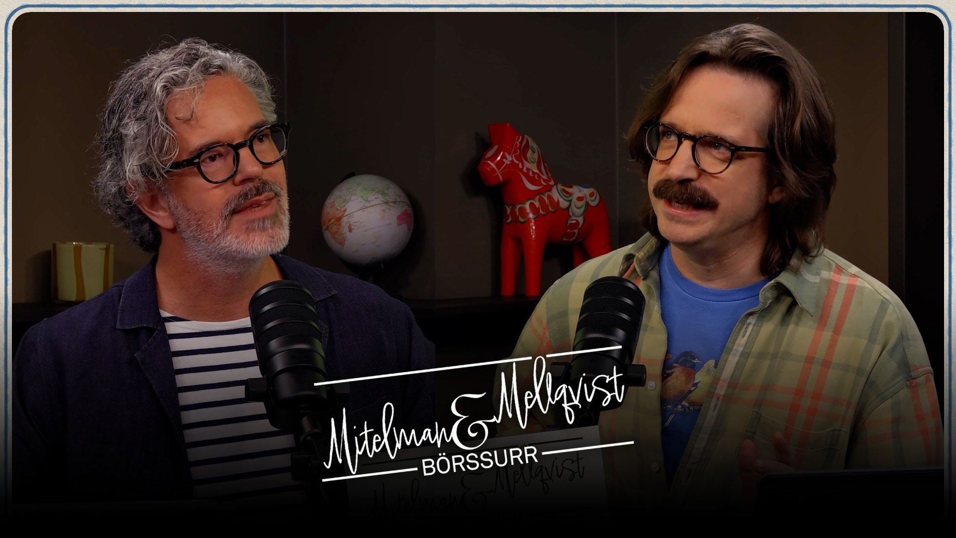 Två män sitter vid mikrofoner i en podcast- eller intervjustudio. De bär glasögon och ser mot sidan. I bakgrunden syns dekorativa föremål.