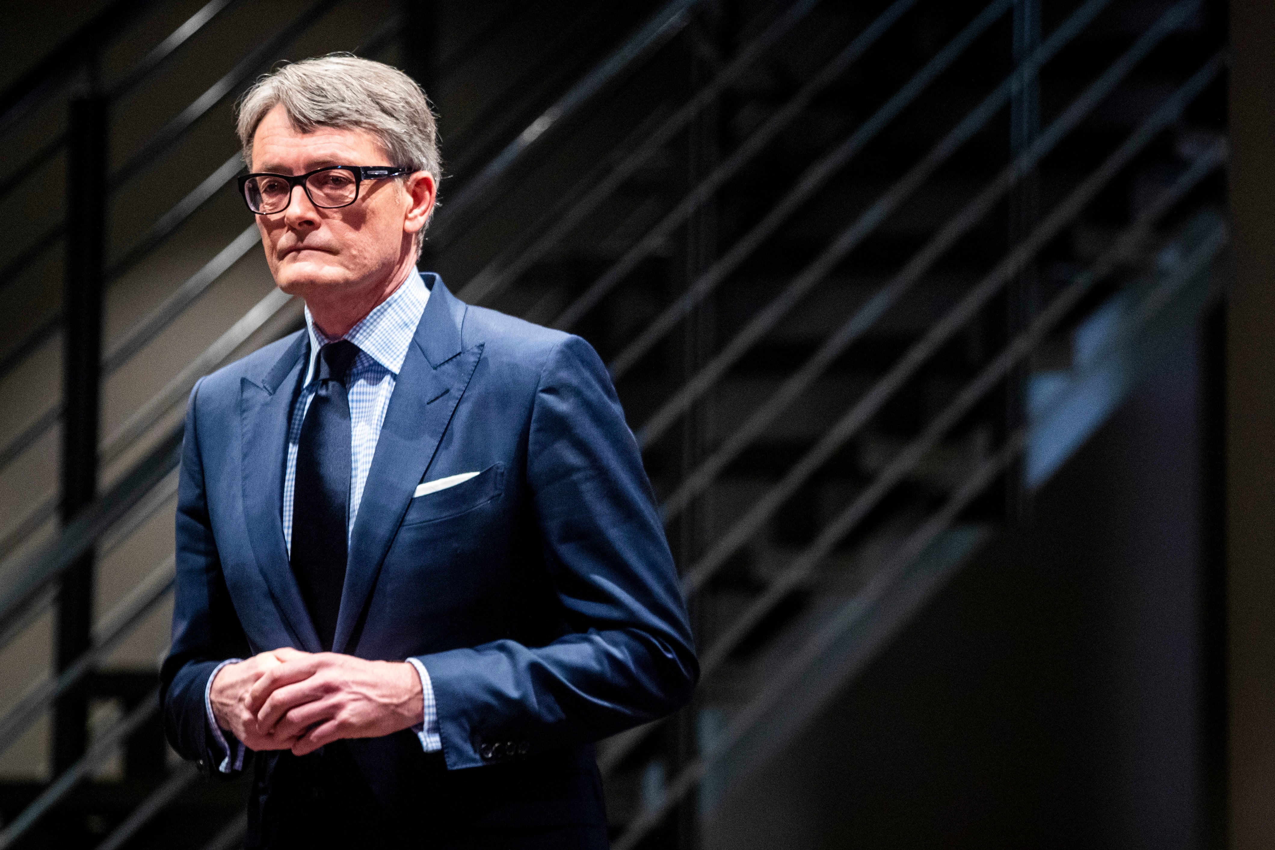 Man i blå kostym och glasögon framför en mörk vägg