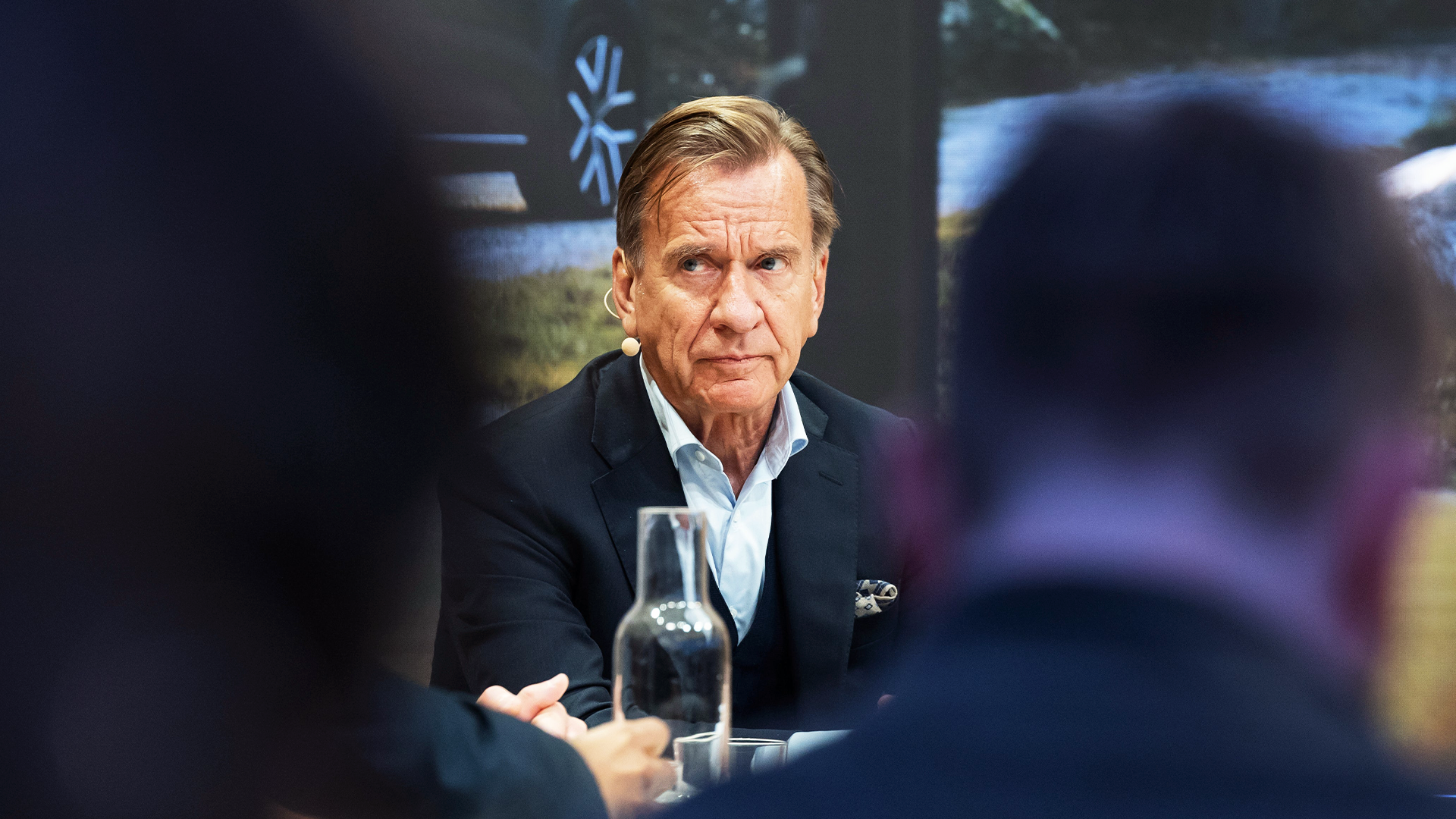 Håkan Samuelsson, klädd i mörk kavaj, sitter vid ett bord och tittar allvarligt åt sidan under ett möte.