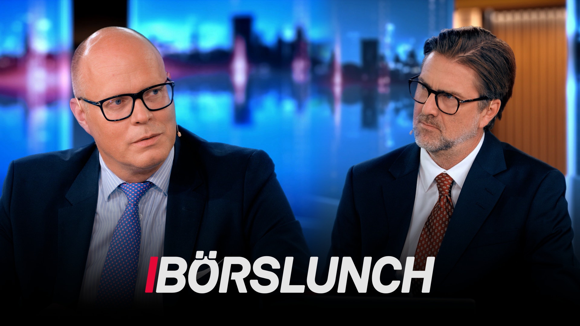 Två män i kostym sitter framför en blurrig stadshorisont. Texten Börslunch visas längst ner på skärmen.