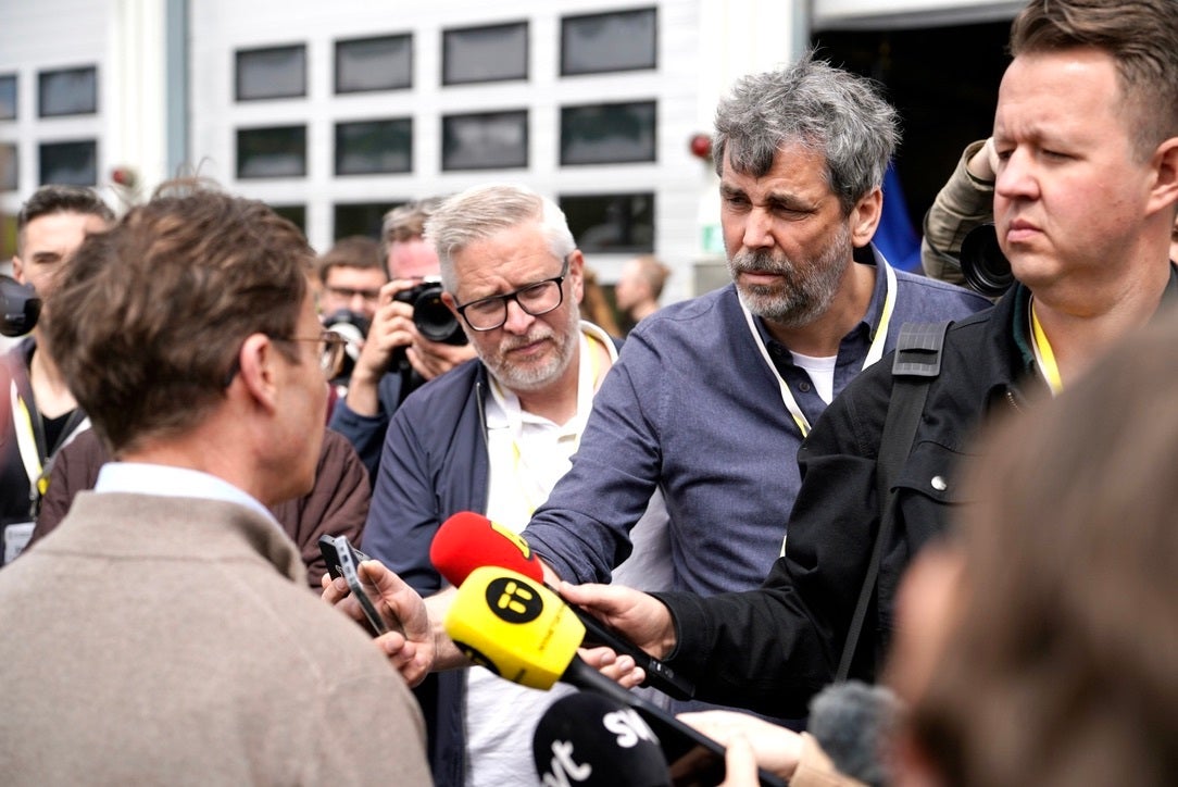 Journalister samlas runt en man och riktar mikrofoner och mobiler mot honom under en intervju utomhus.