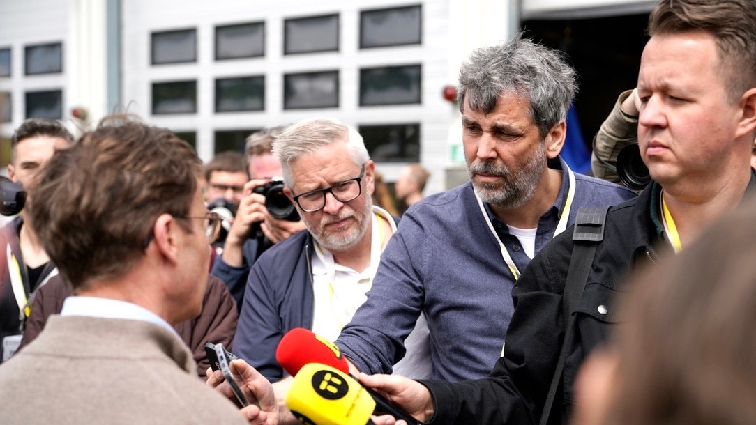 Journalister samlas runt en man och riktar mikrofoner och mobiler mot honom under en intervju utomhus.