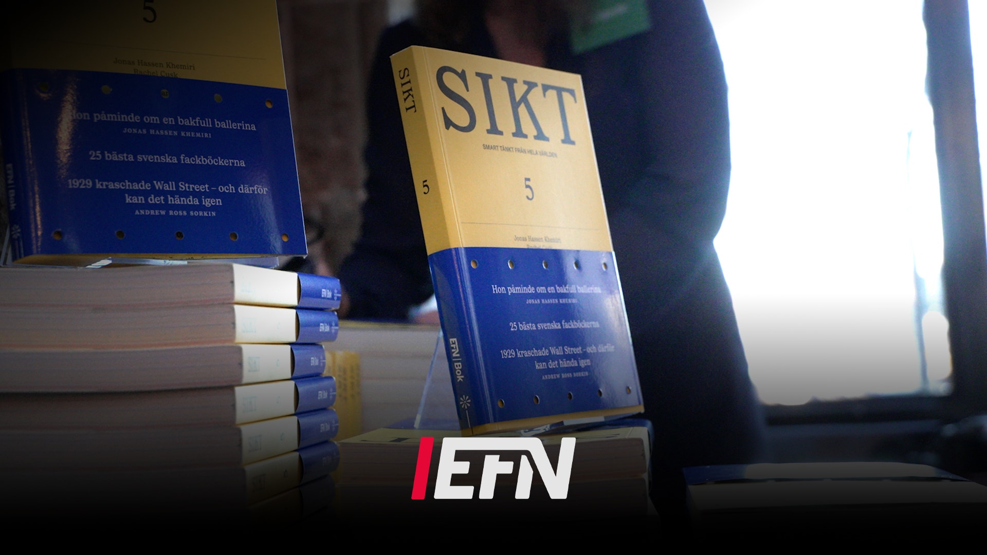 Bok med titeln SIKT nummer 5, blå och gul omslag, fotograferad tillsammans med flera staplade exemplar av samma bok.