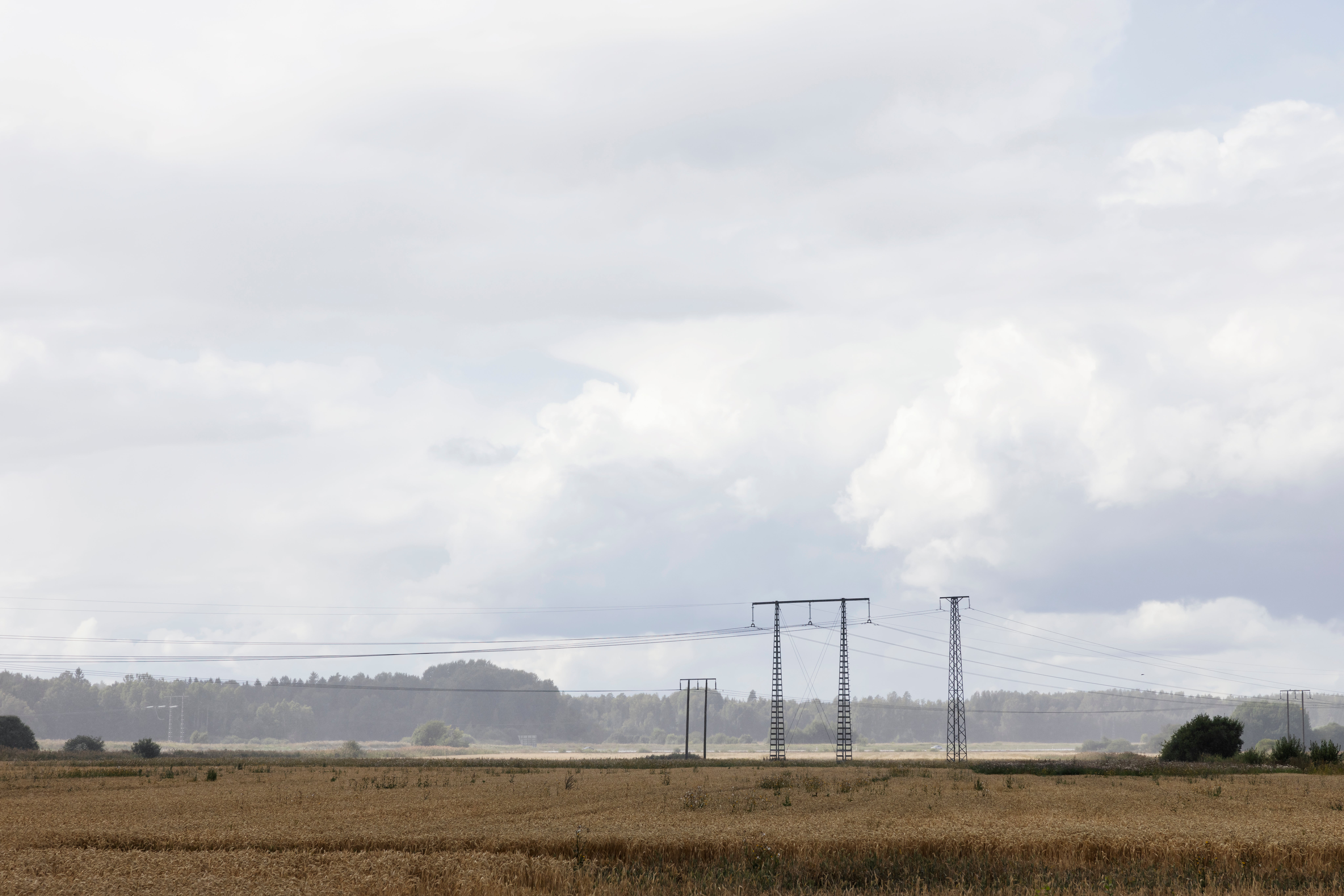 Öppet jordbrukslandskap med kraftledningar som sträcker sig över ett plöjt fält under molnig himmel.