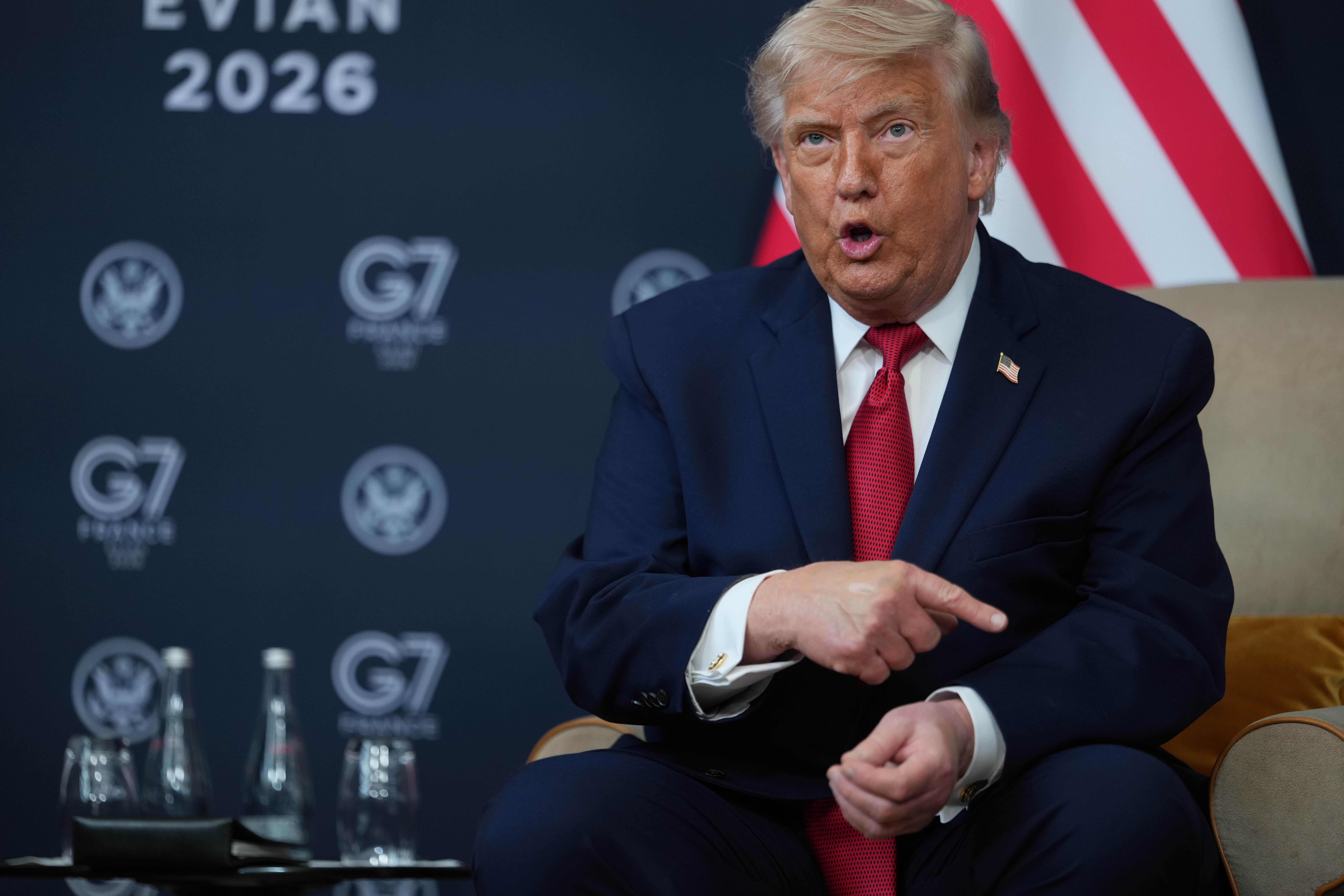 Man i mörkblå kostym och röd slips talar vid ett G7-möte i Evian 2026, med den amerikanska flaggan i bakgrunden.