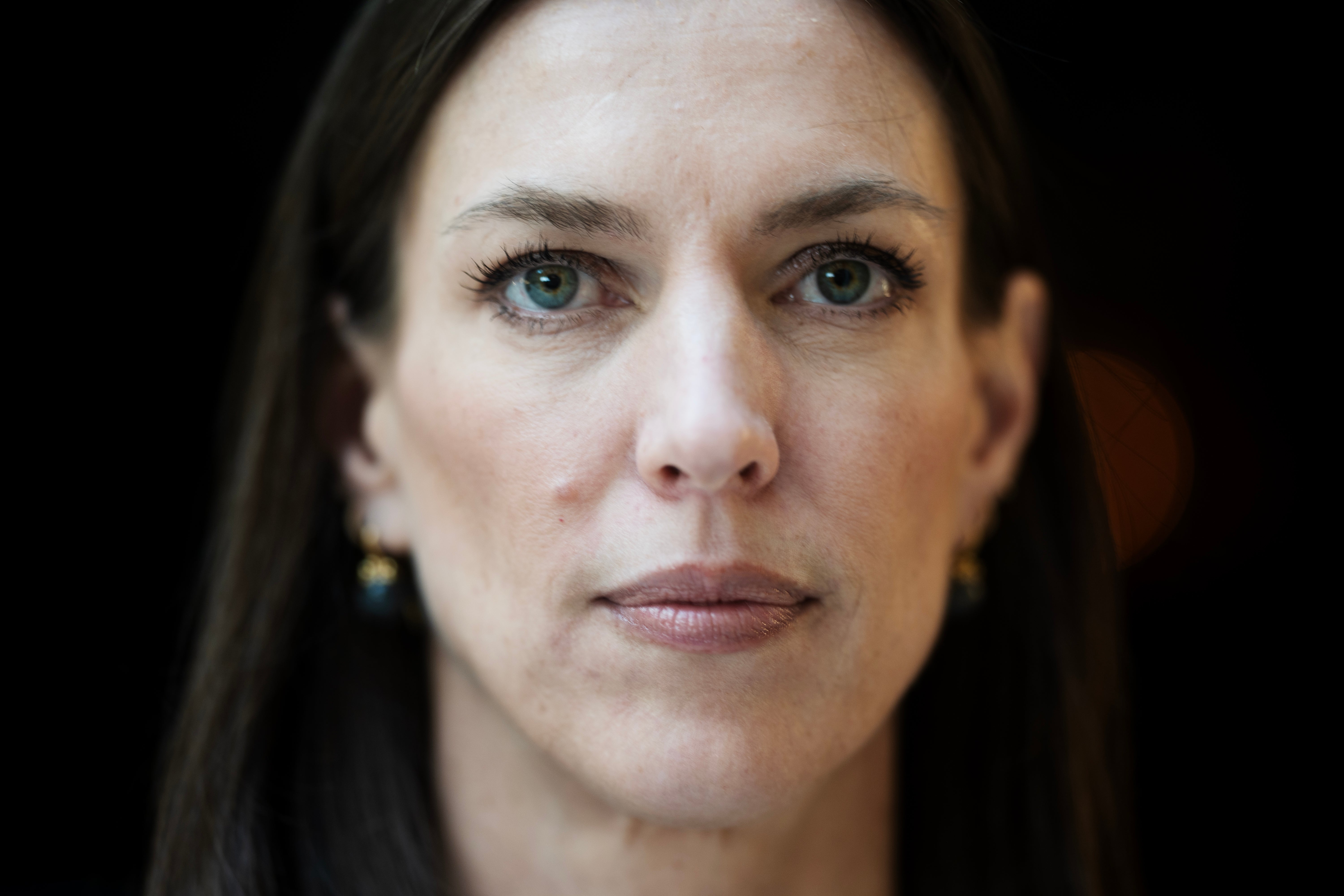 Porträttfoto av en kvinna med mörkt hår mot mörk bakgrund.