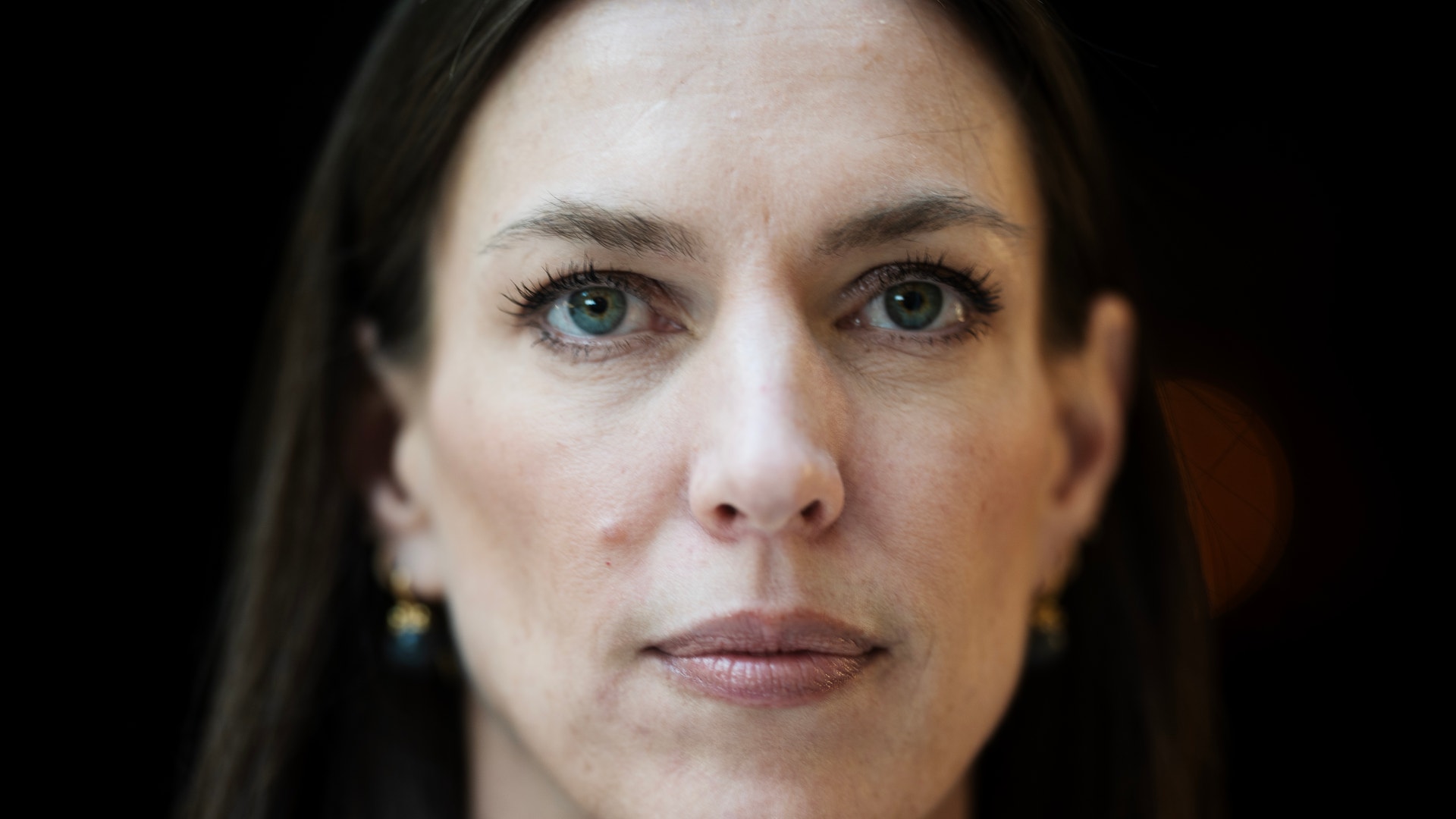 Porträttfoto av en kvinna med mörkt hår mot mörk bakgrund.