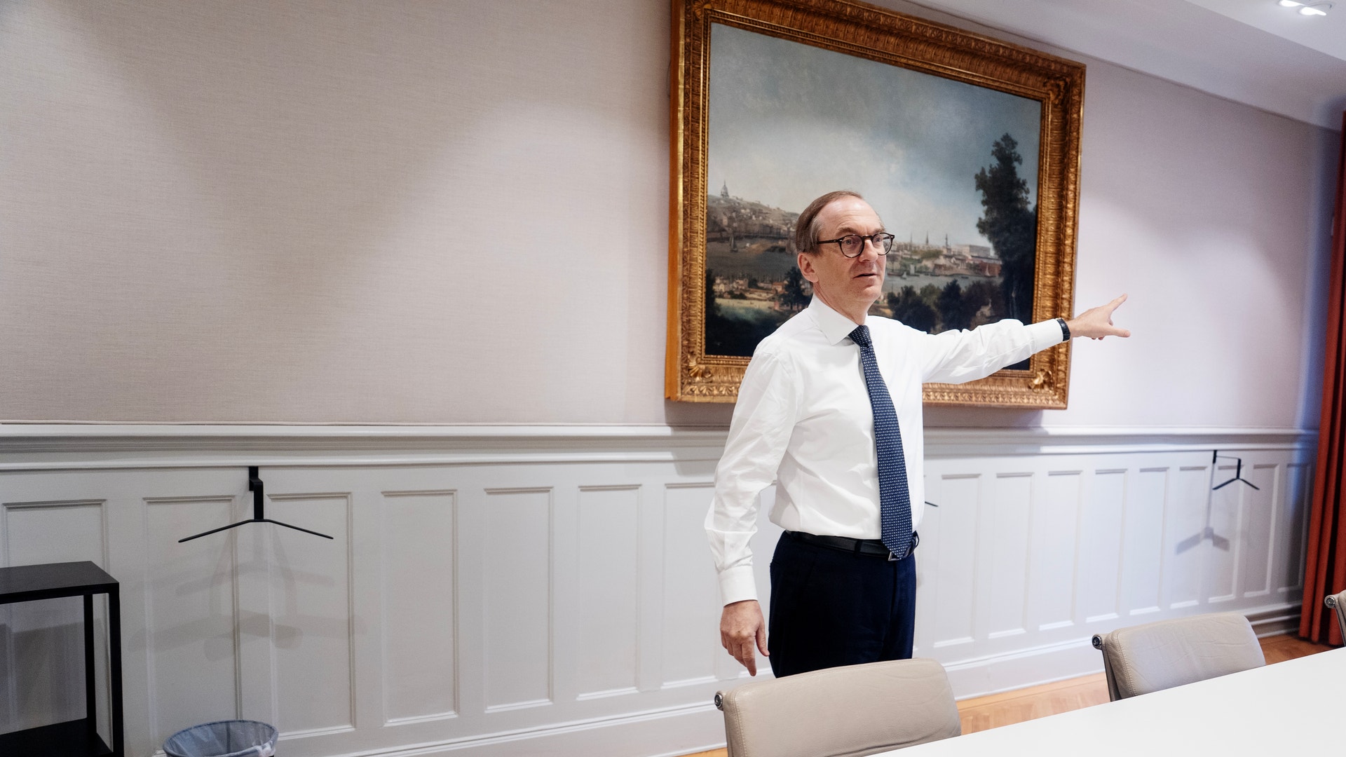 Man i vit skjorta och slips gestikulerar i ett modernt kontor