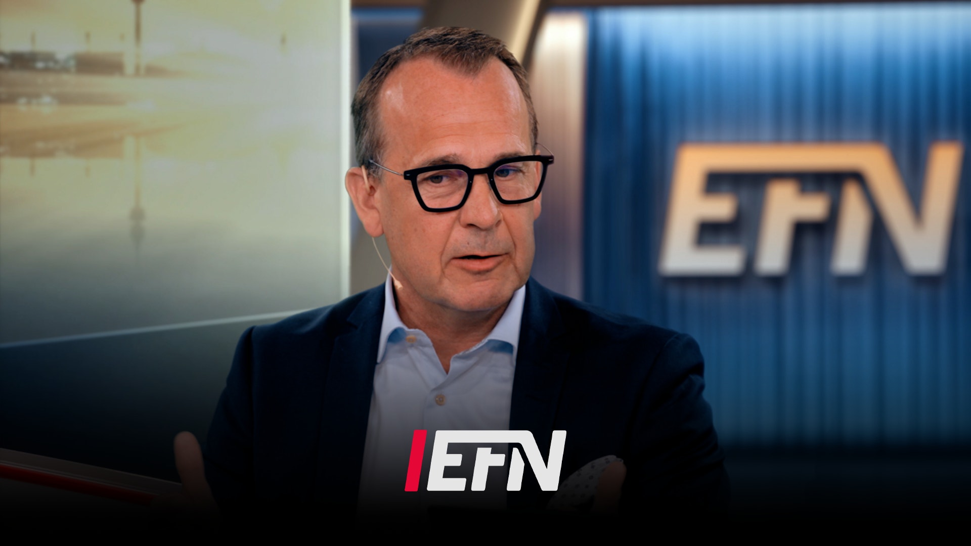 Man i glasögon och mörk kavaj sitter framför studiobakgrund med EFN-logon