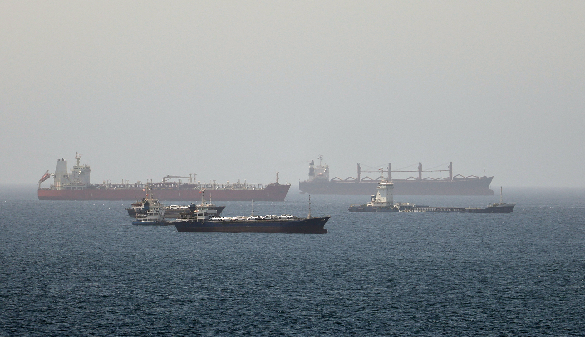 Tre stora lastfartyg på öppet hav vid Hormuz-sundet. Ett rött tankfartyg i bakgrunden, ett svart containerfartyg i förgrunden och ett större lastfartyg till höger.