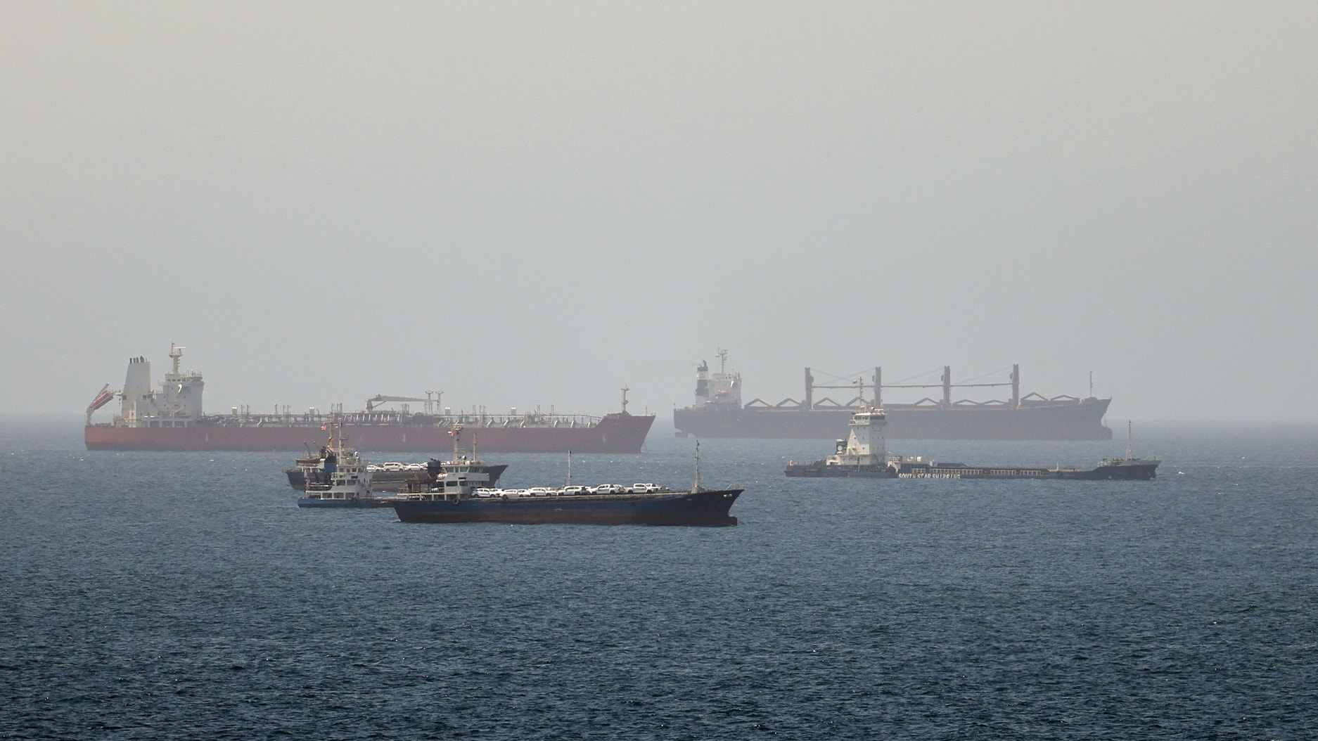 Tre stora lastfartyg på öppet hav vid Hormuz-sundet. Ett rött tankfartyg i bakgrunden, ett svart containerfartyg i förgrunden och ett större lastfartyg till höger.