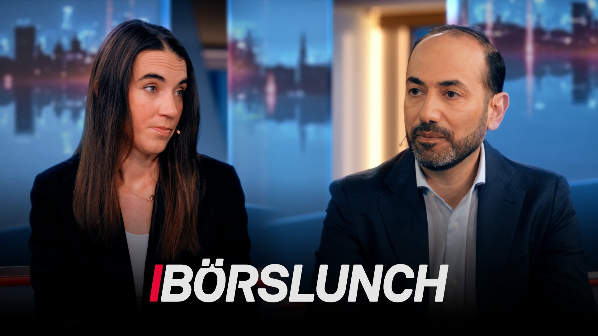 Två personer i affärskläder framför en stadsskyline i en TV-studio för programmet Börslunch.