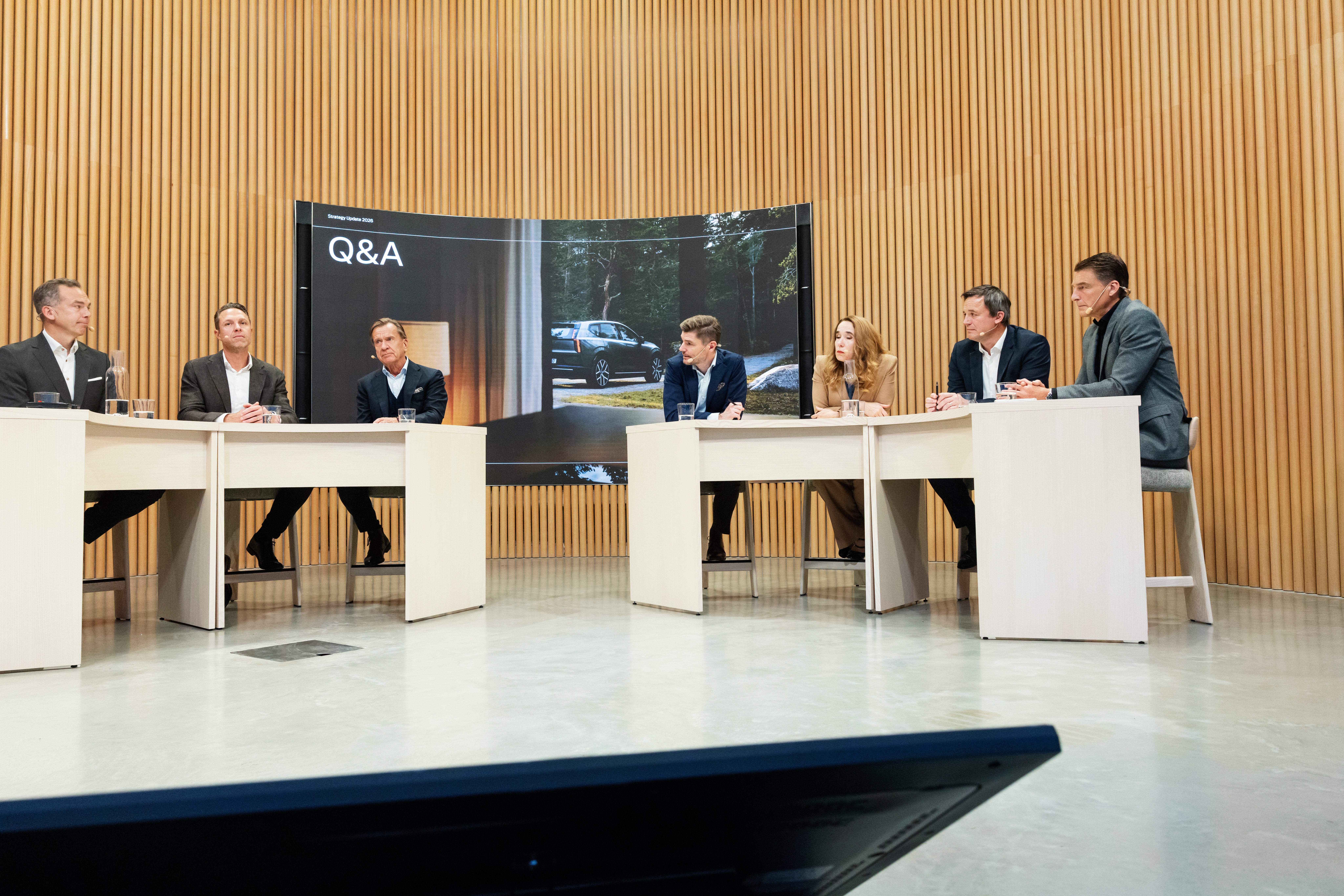 Sju personer sitter vid bord i en pressträff med en skärm som visar texten Q&A i bakgrunden.