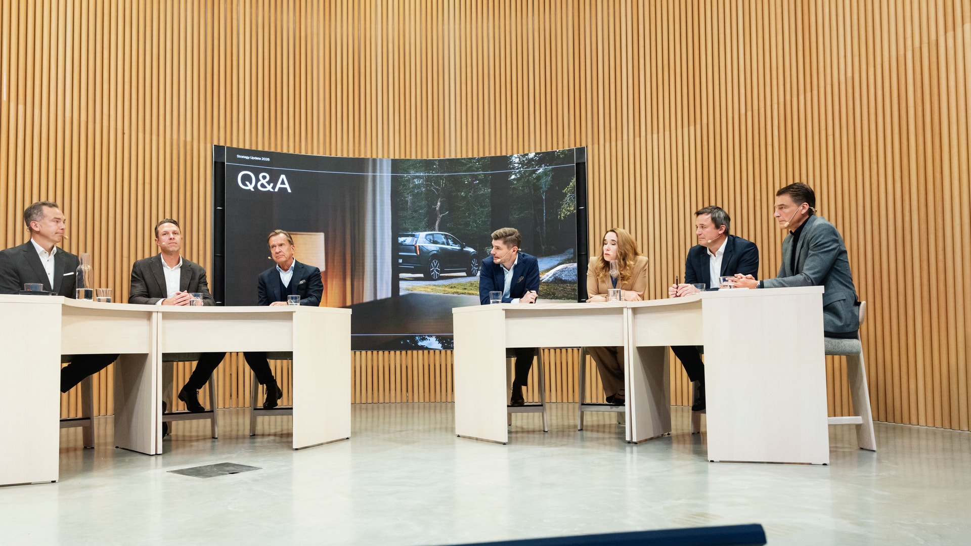 Sju personer sitter vid bord i en pressträff med en skärm som visar texten Q&A i bakgrunden.