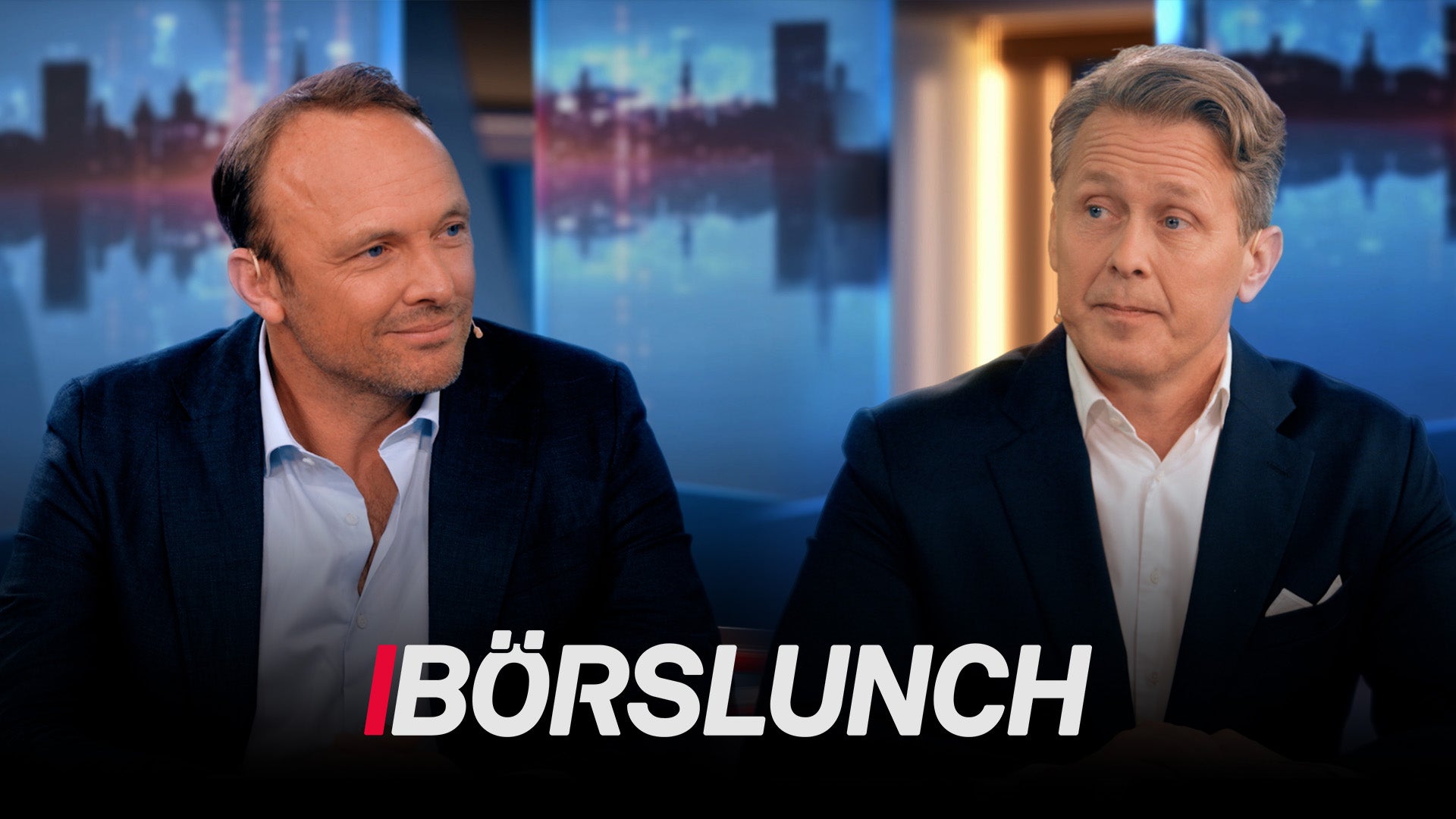 Två män i kostym under en tv-intervju med stadshorisont i bakgrunden