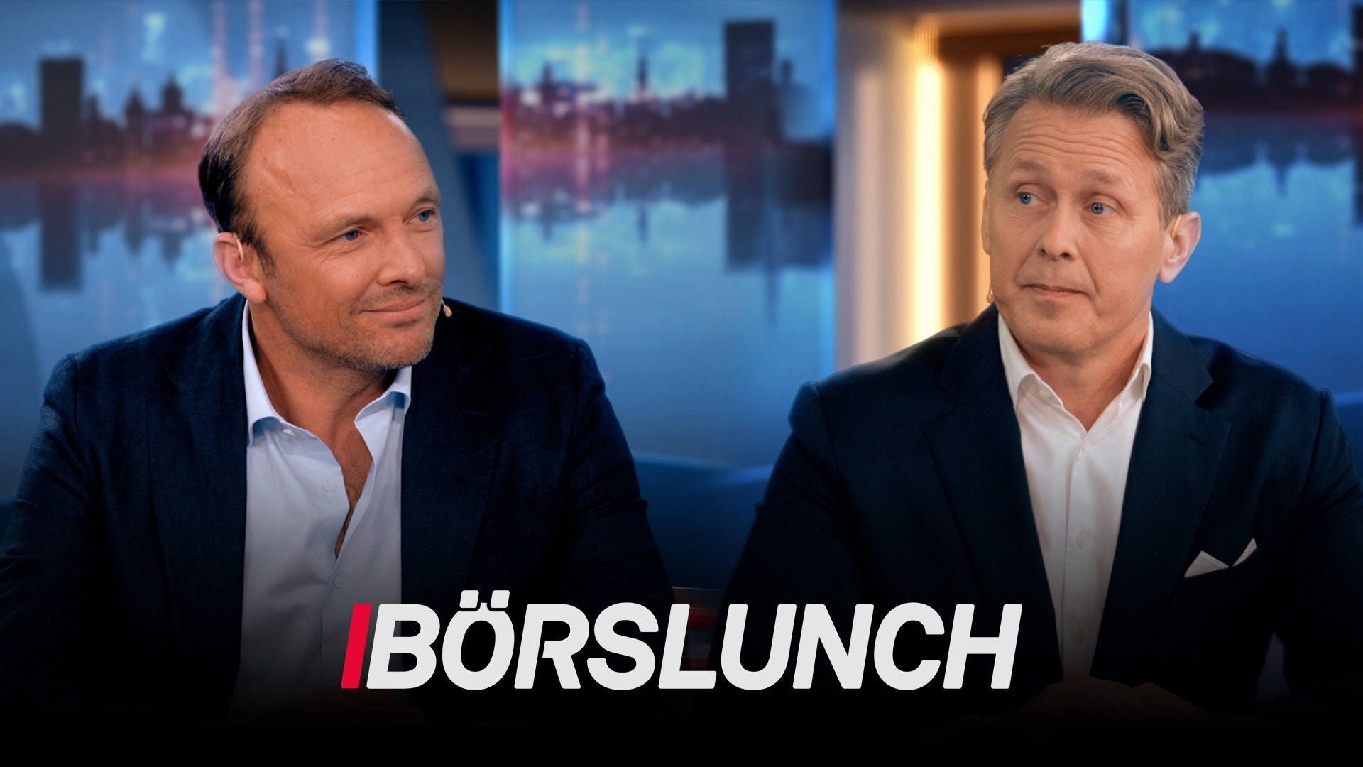 Två män i kostym under en tv-intervju med stadshorisont i bakgrunden