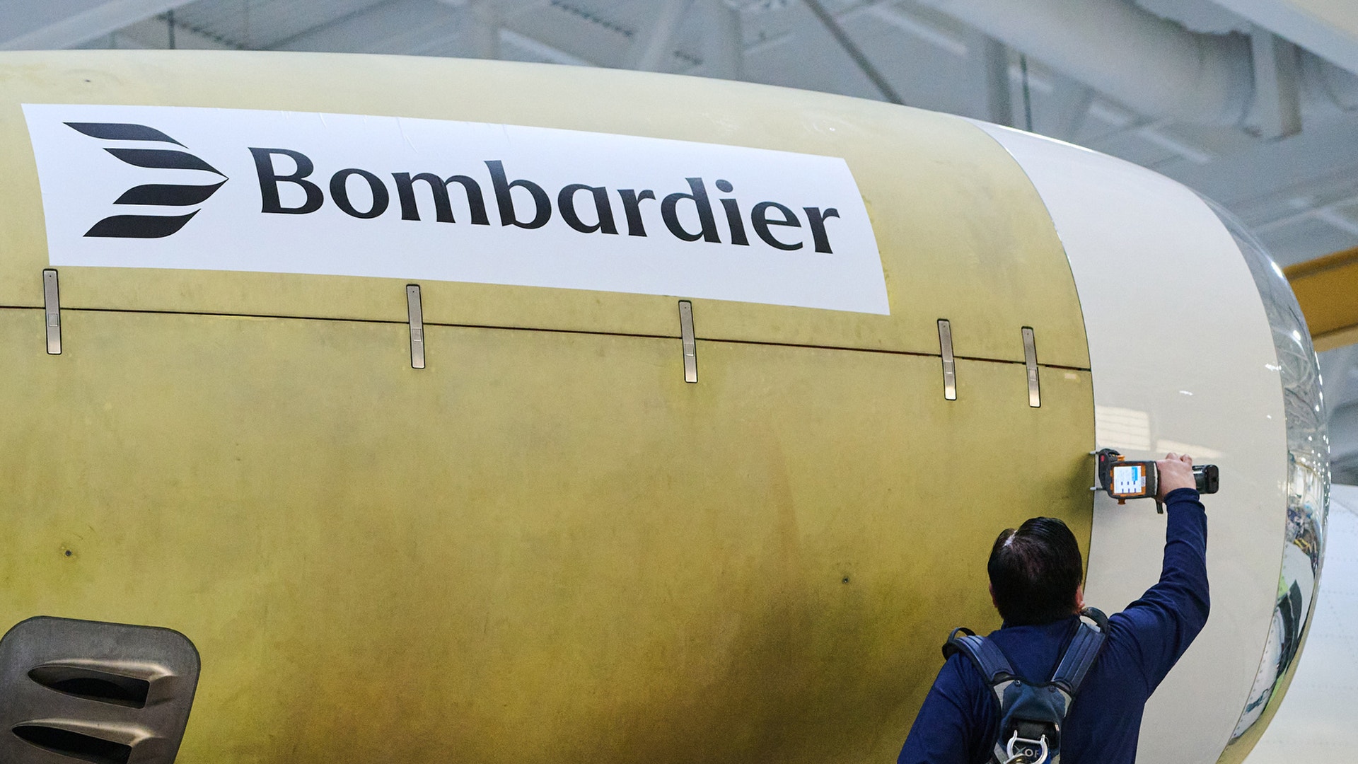 En person fotograferar en gul flygplansfuselage märkt med Bombardier-logon.