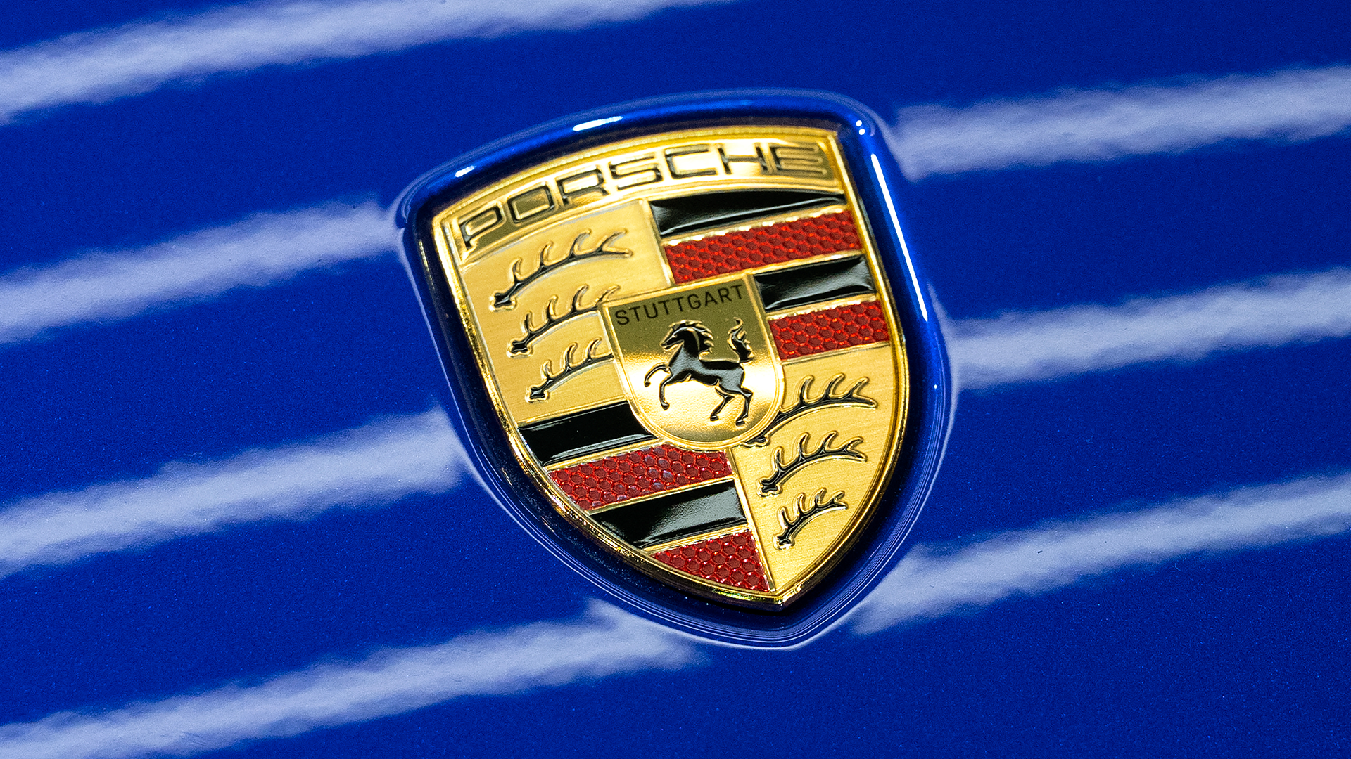 Porsches guldfärgade emblem med en springande häst på en blå bilkaross.