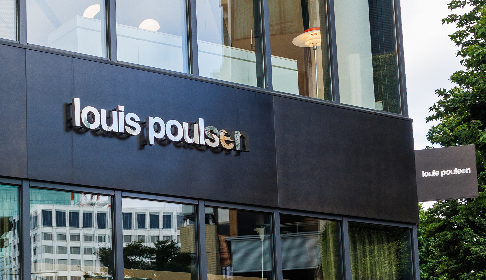 Fasad på Louis Poulsen-butik med svart vägg och vit logotyp på en modern byggnad med glasfönster.