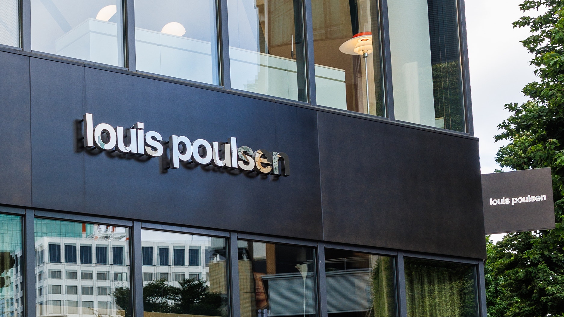 Fasad på Louis Poulsen-butik med svart vägg och vit logotyp på en modern byggnad med glasfönster.