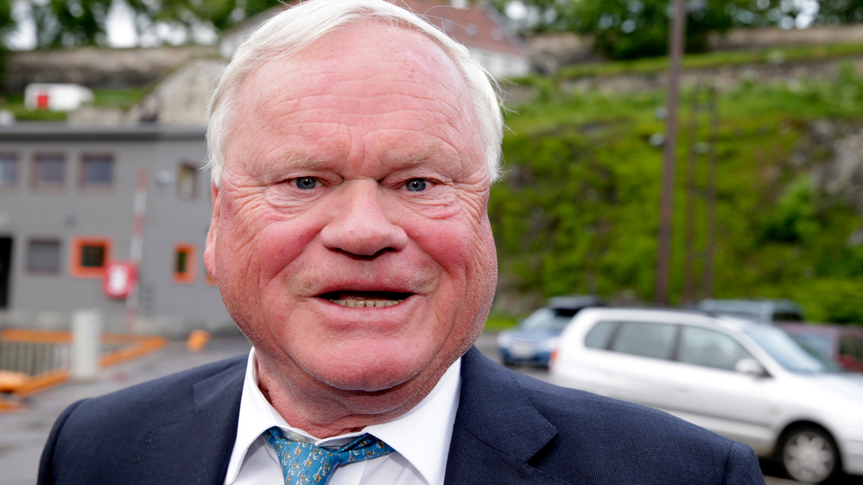 Porträtt av en äldre man med vit hår, mörk kostym och blå slips.