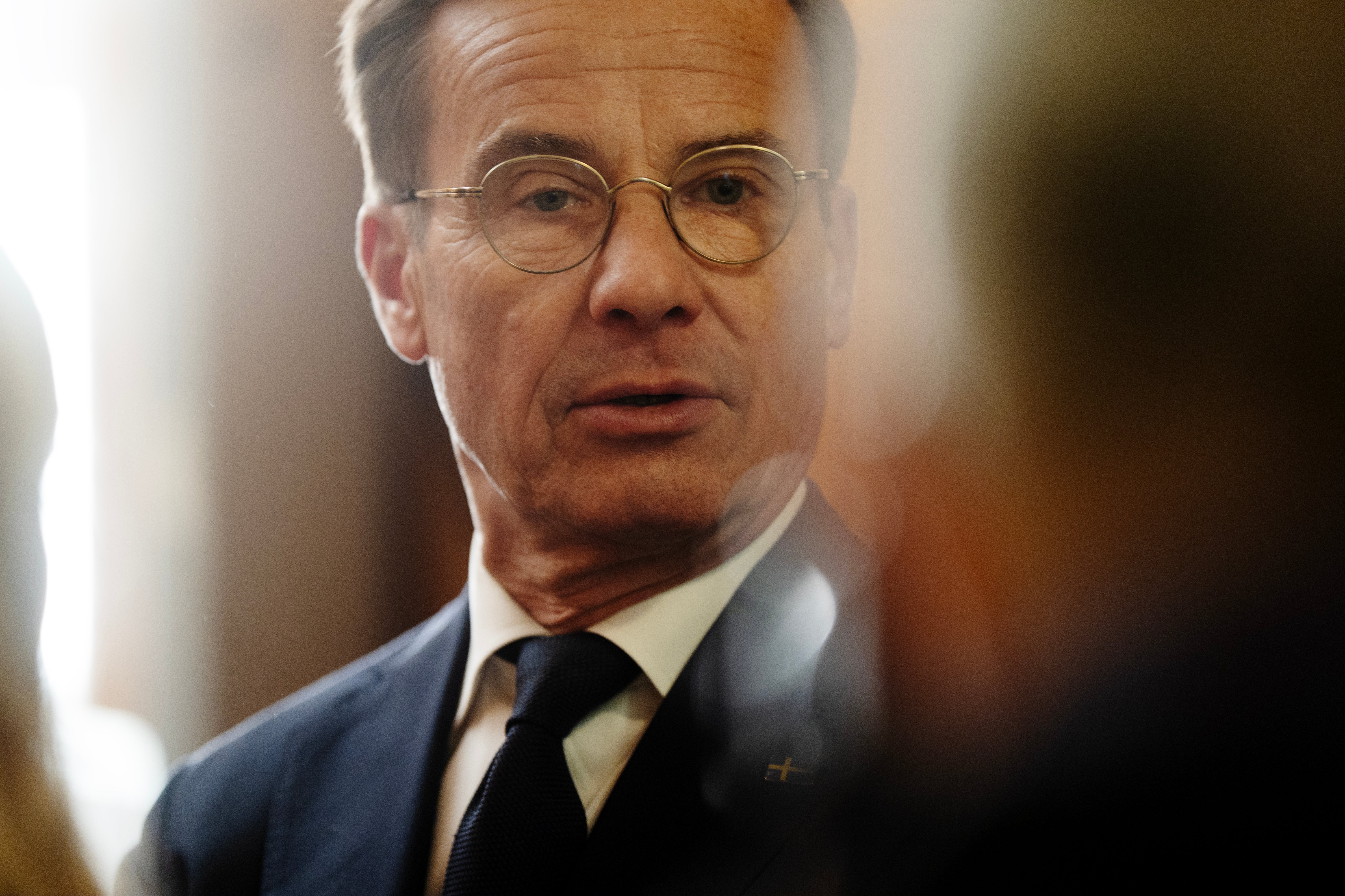 Man med glasögon och kostym pratar med människor omkring sig.